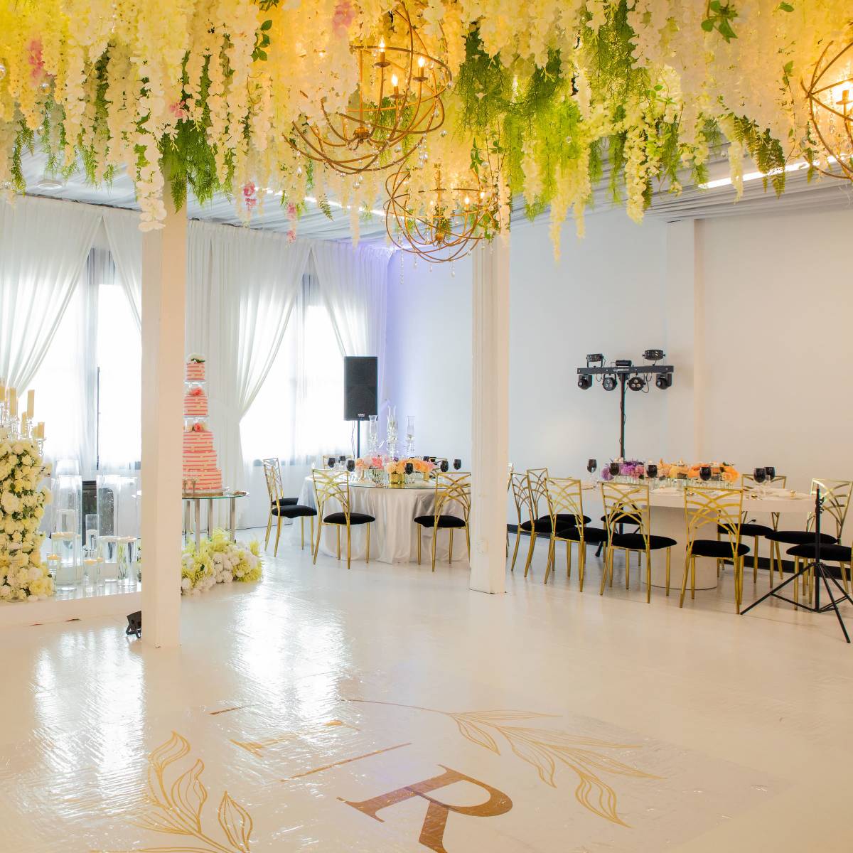 A beautifully decorated event space with floral arrangements hanging from the ceiling, a cake display, and elegantly set tables.
