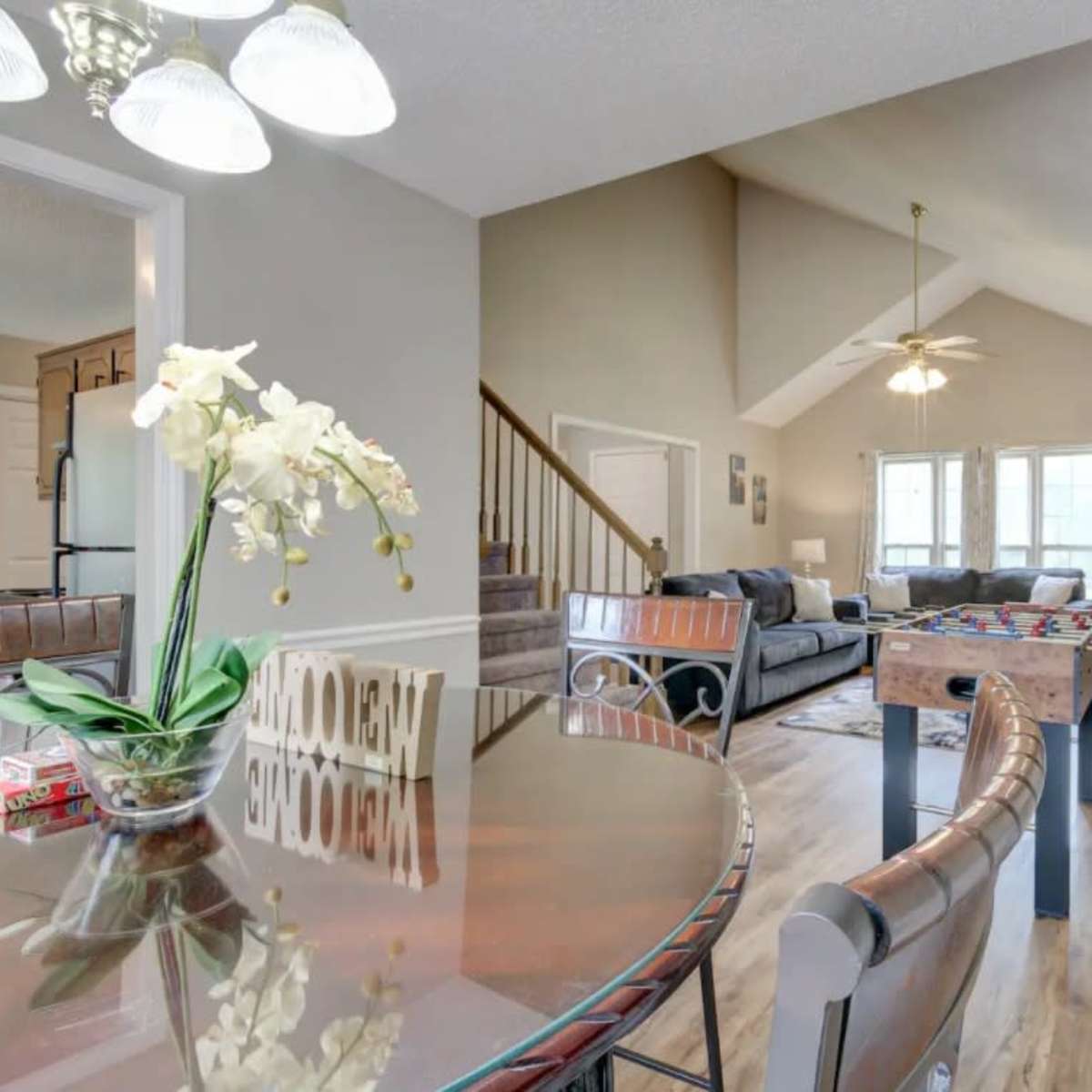 A spacious living area with a dining table in the foreground, a foosball table in the middle, and a comfortable seating area with a large sofa in the background.