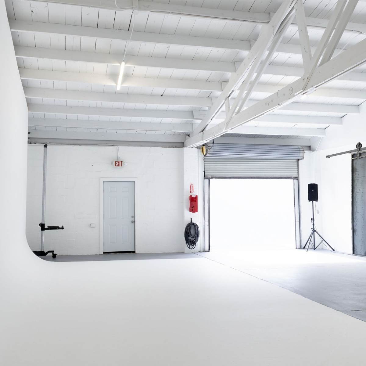 A spacious, empty studio with white walls, a concrete floor, and large industrial-style doors.