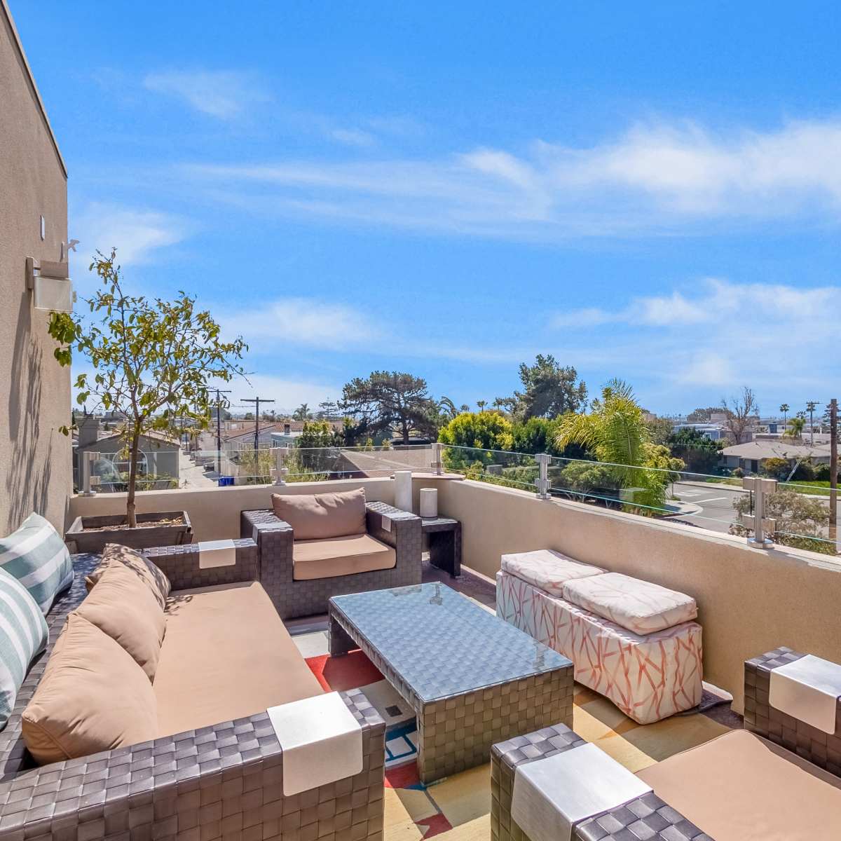 A rooftop terrace with brown wicker furniture, a glass coffee table, and a clear blue sky above.