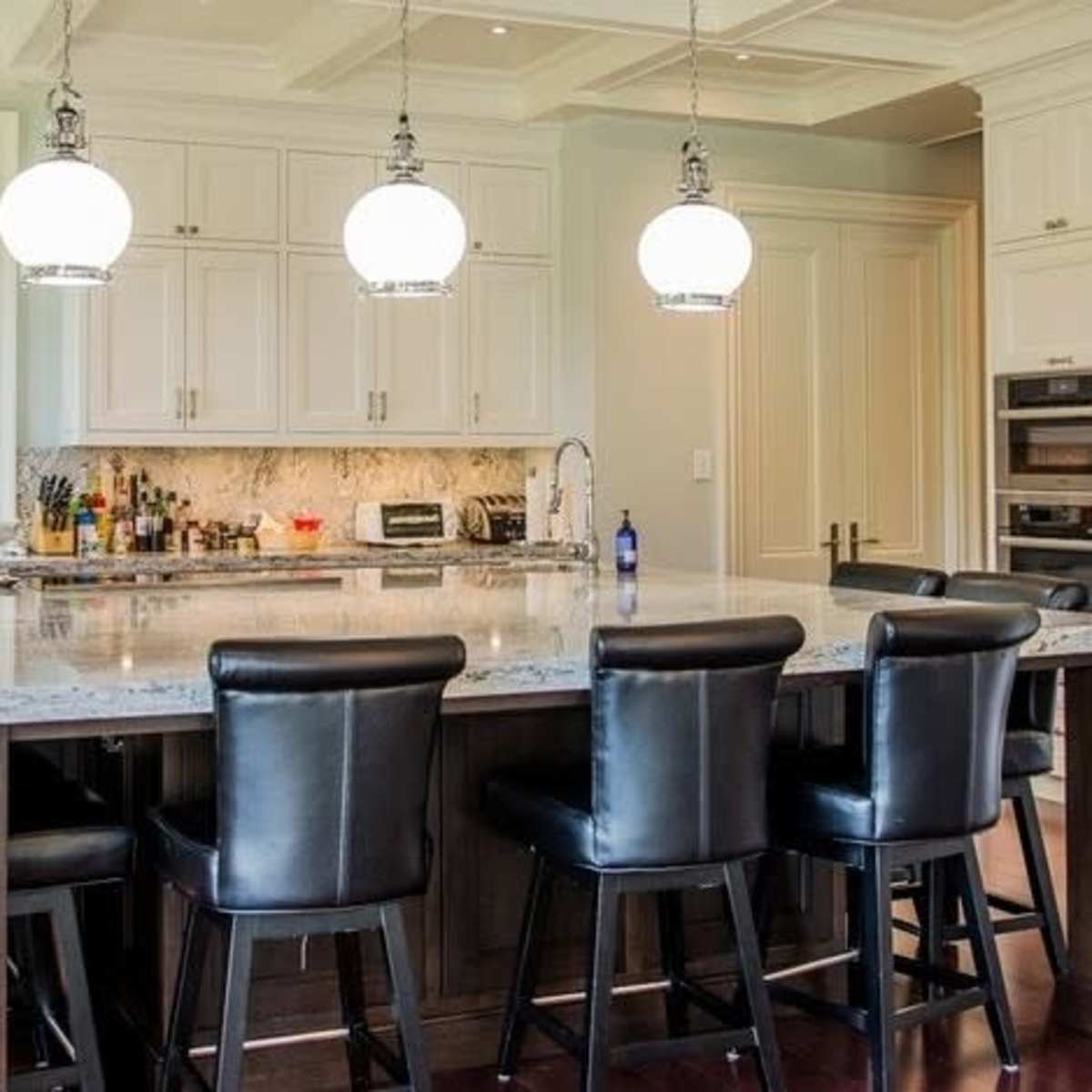 A modern kitchen features a large island with seating, white cabinetry, and pendant lighting above.
