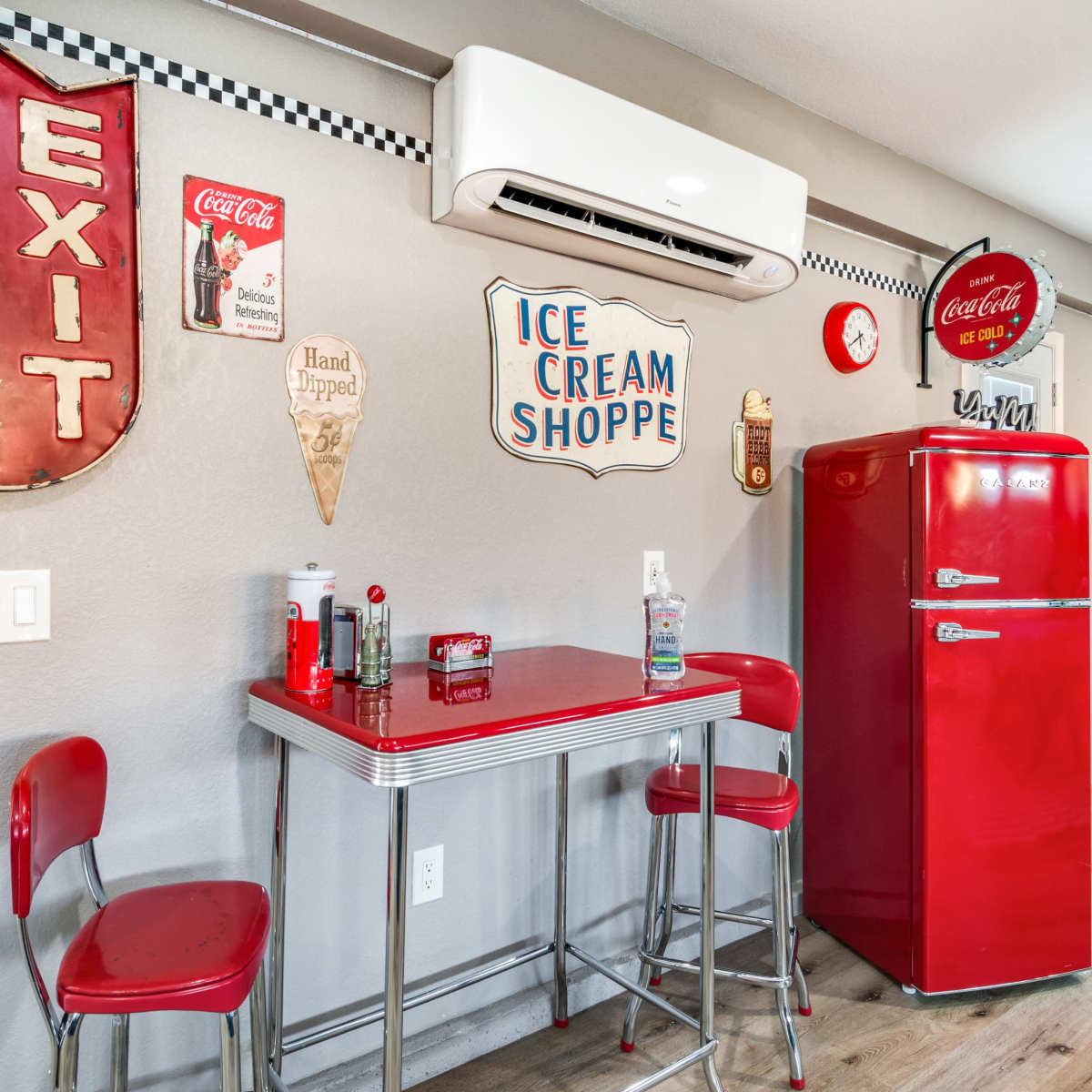A retro-style kitchen corner with a red fridge, red stools, and vintage Coca-Cola signs on the walls.