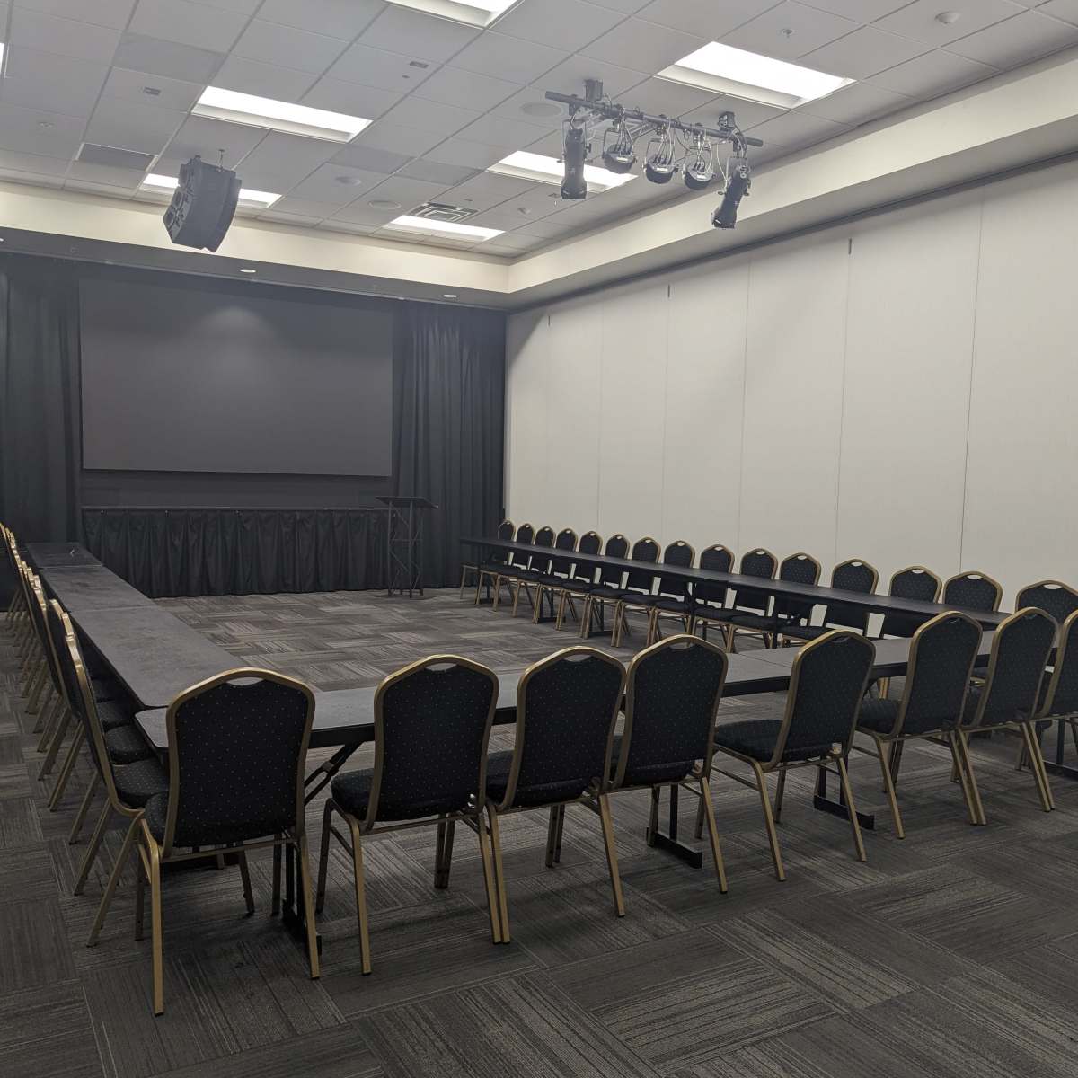 A conference room arranged with a large round table surrounded by chairs, facing a screen at the front.