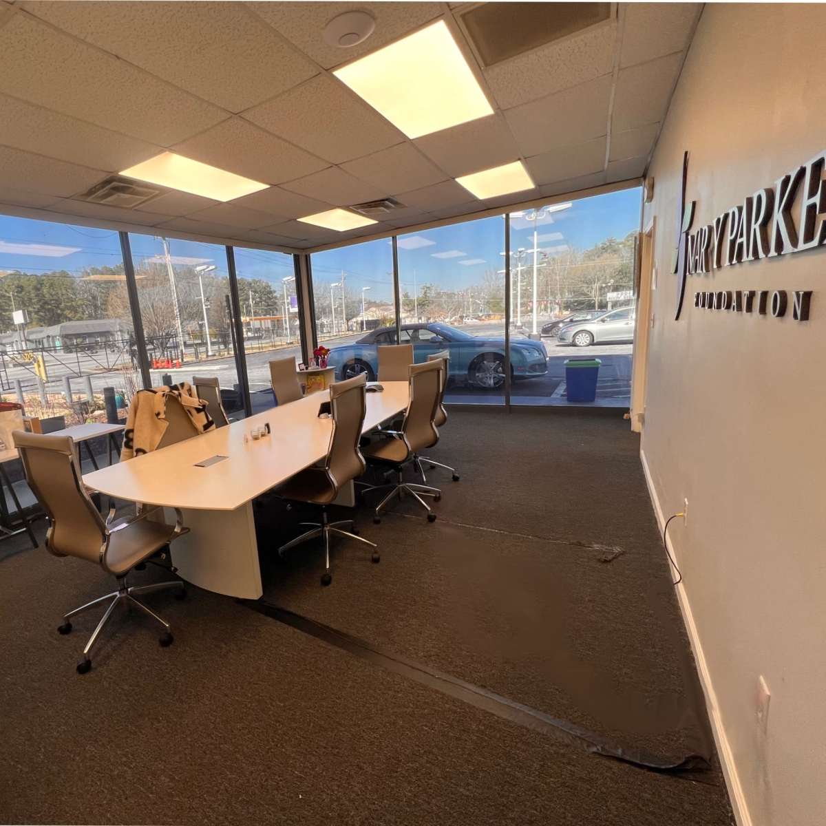A modern office space with several desks, ergonomic chairs, and large windows overlooking an outdoor area.