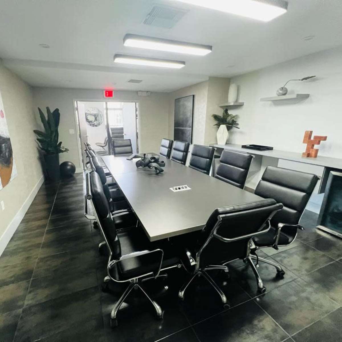 A long conference table surrounded by black leather chairs is featured in a modern meeting room with minimalist decor.
