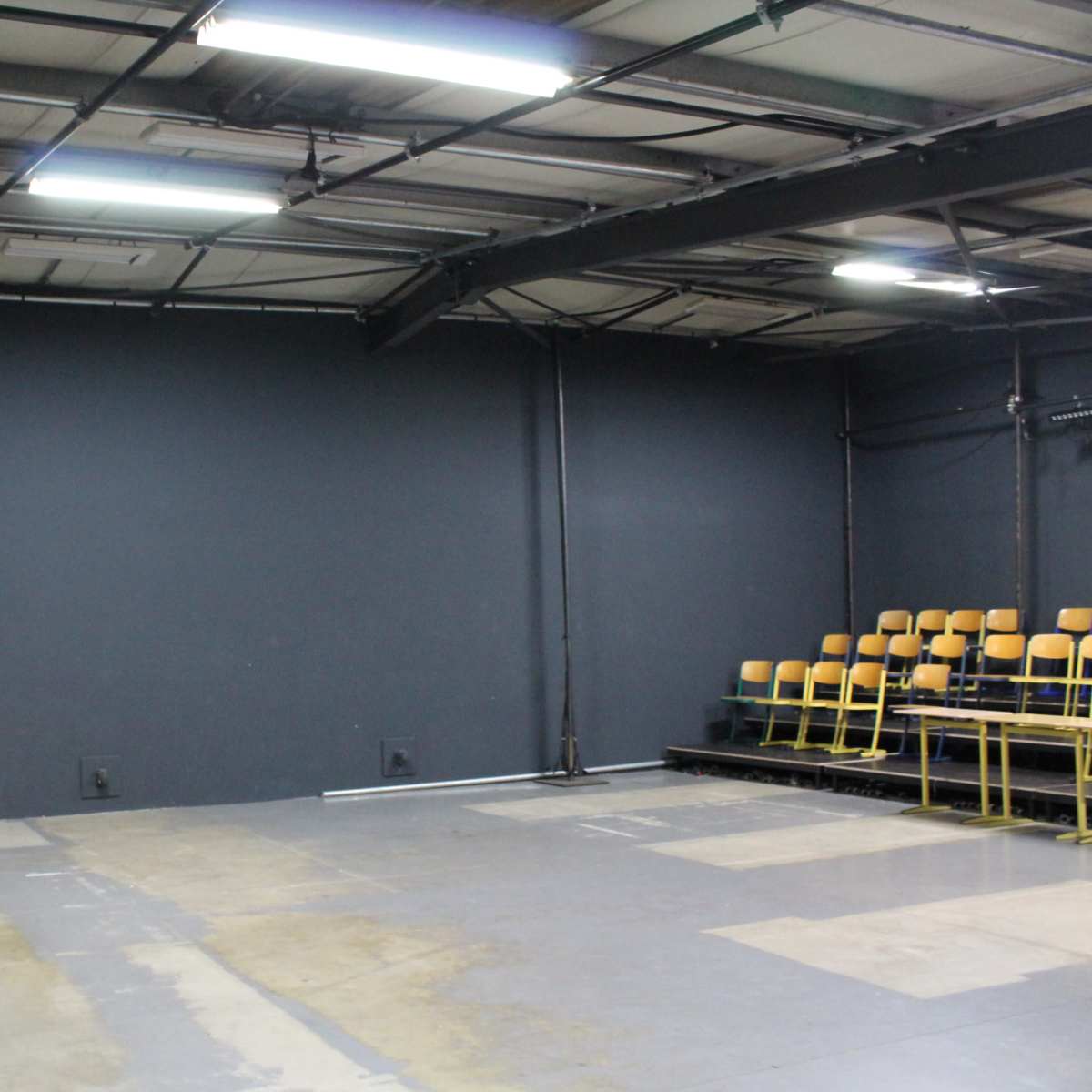 An empty indoor space with a gray wall and a row of yellow chairs against one side.