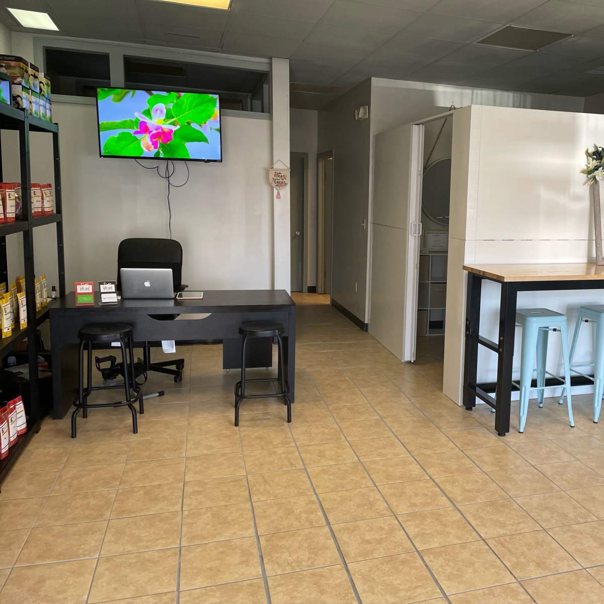 A spacious interior of a commercial space featuring a reception area with a desk and a TV, alongside a dining area with a long table and stools.