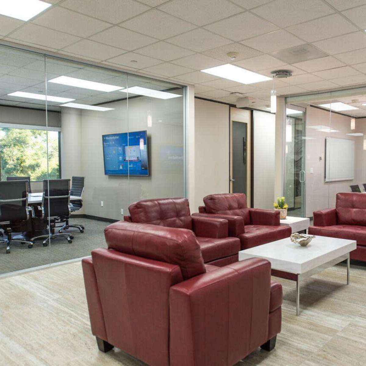A modern office space with a seating area featuring red chairs, a coffee table, and a glass-walled conference room in the background.