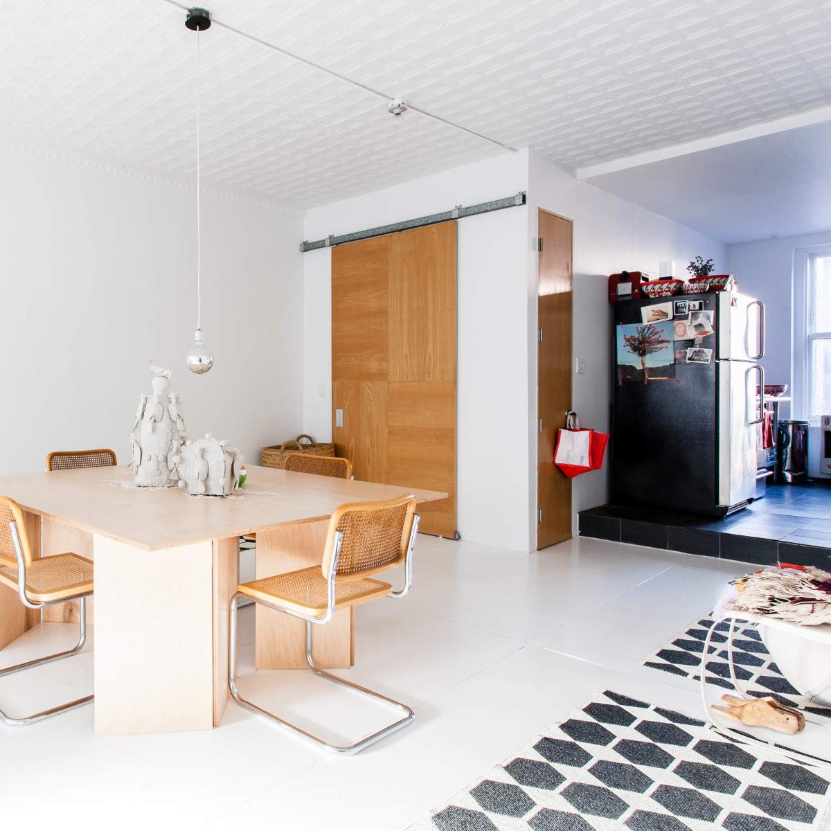 A spacious, bright dining area with a wooden table surrounded by four chairs, complemented by contrasting black and white patterned rugs.