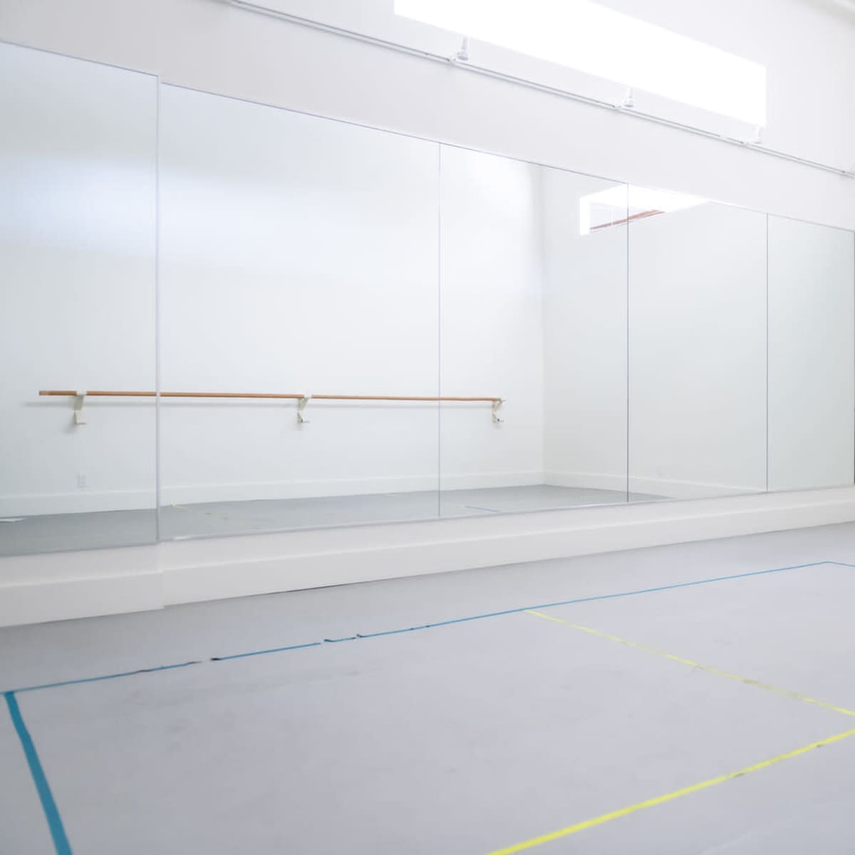 A spacious, brightly lit dance studio featuring large mirrors and a wooden barre along one wall.