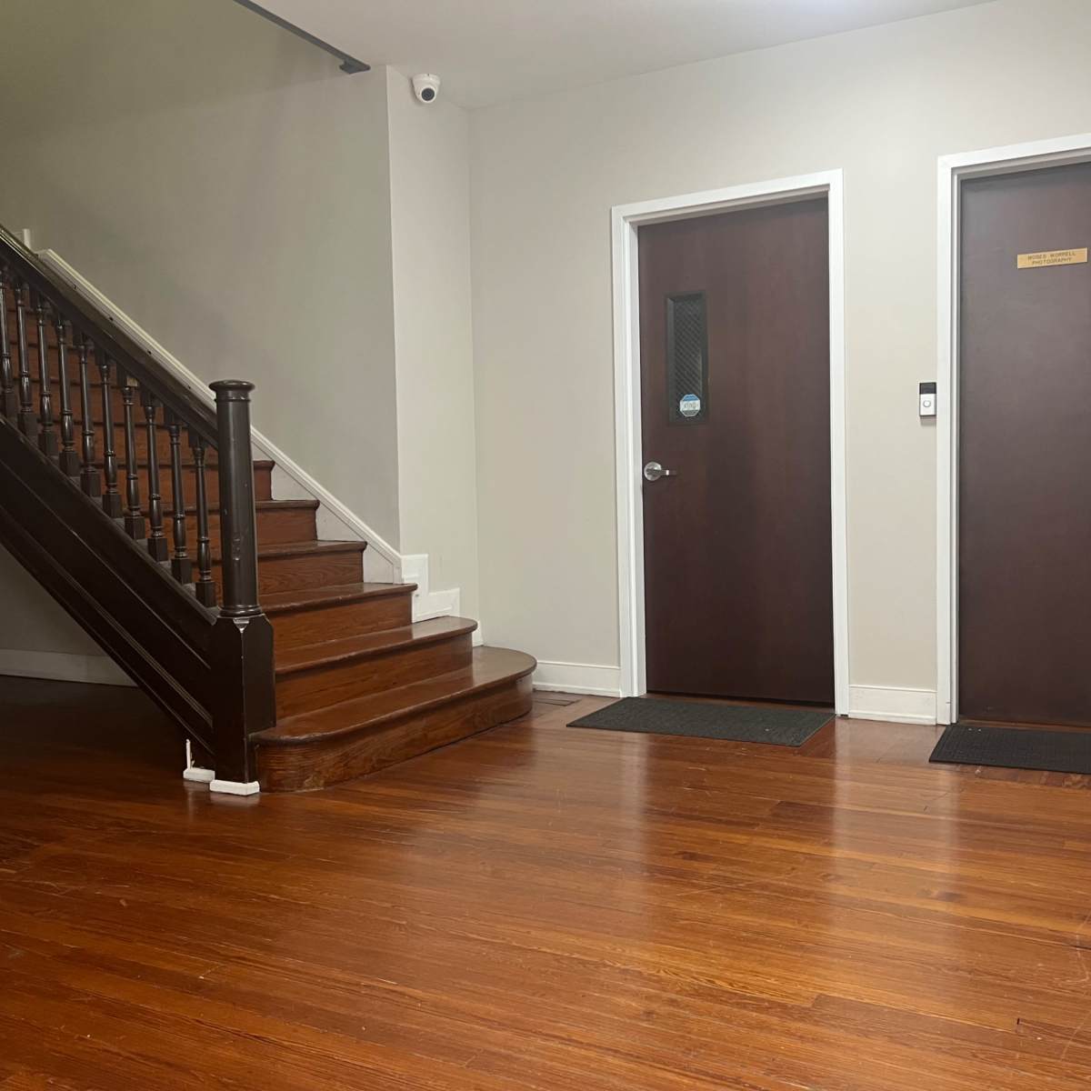 A hardwood-floored hallway with a staircase on the left and two closed doors on the right, labeled with the numbers 210.