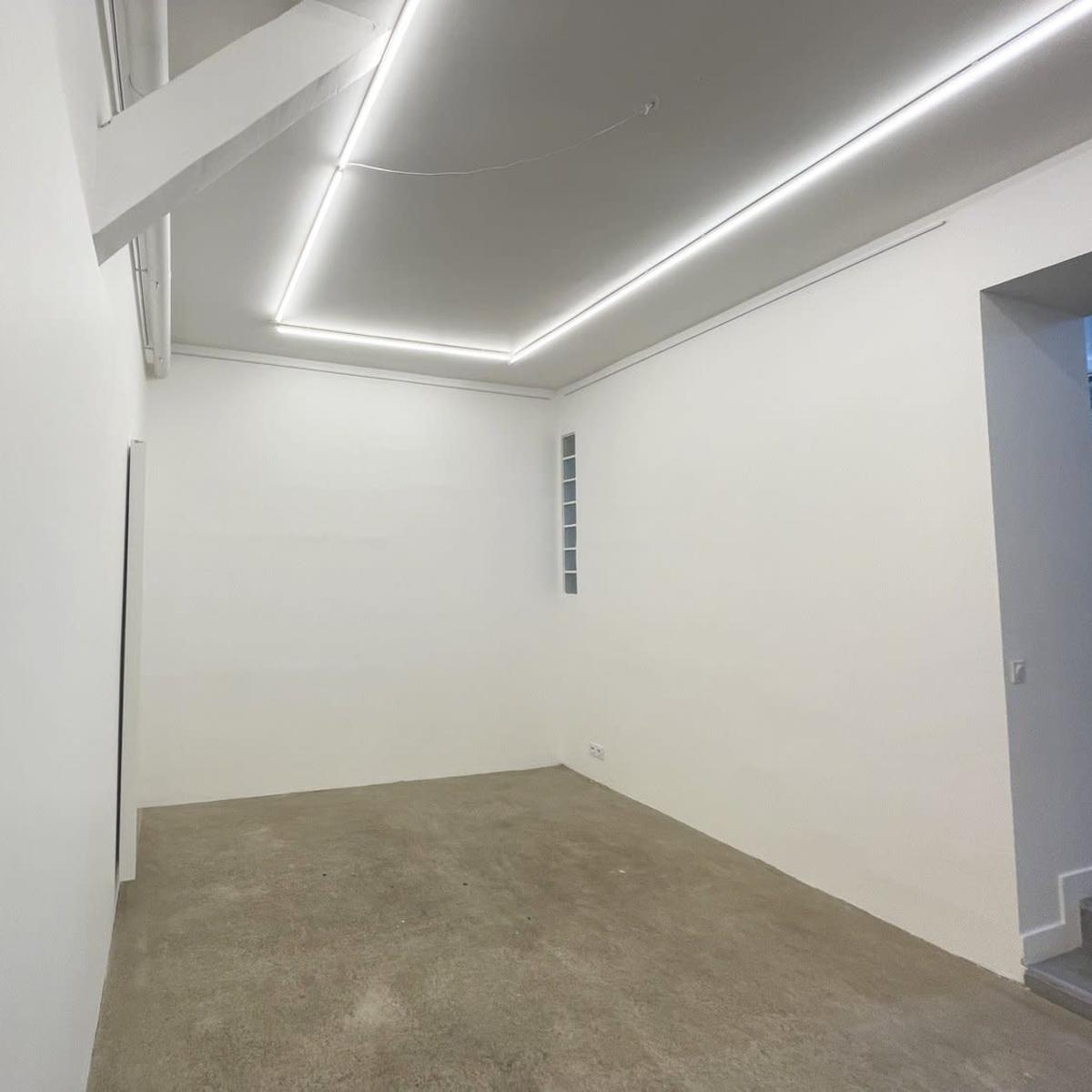 An empty, white-walled room with a concrete floor and overhead LED lighting.