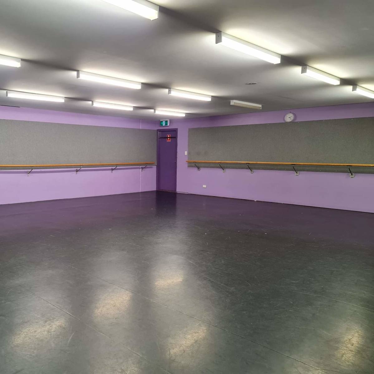 An empty dance studio with purple walls, a smooth black floor, and mirrored panels along the walls.