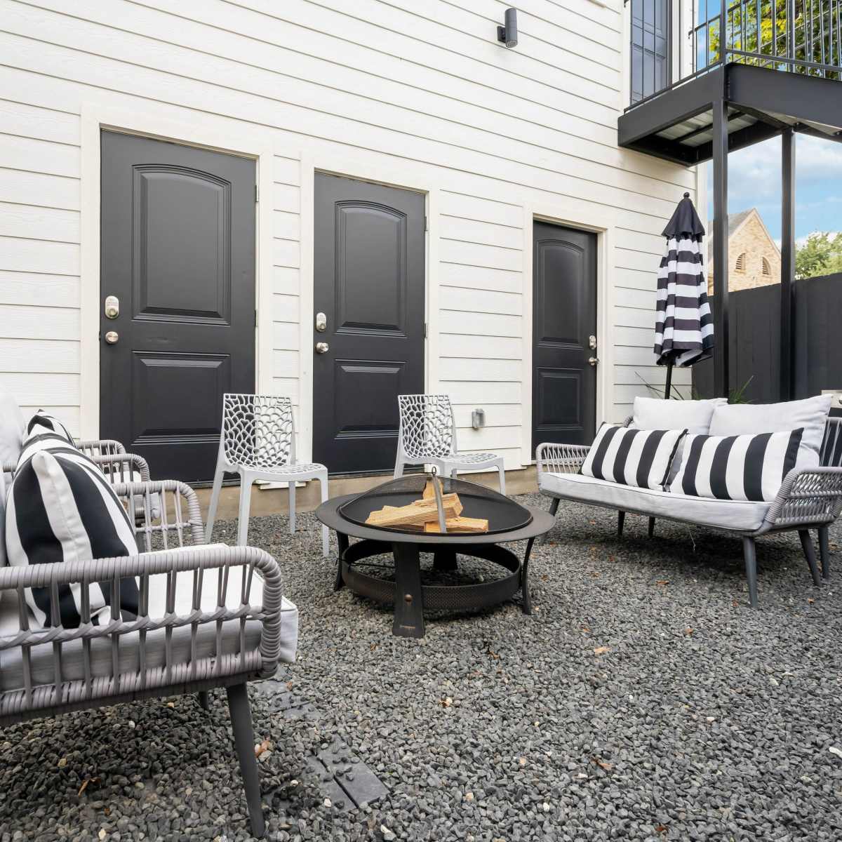 A small outdoor seating area with two couches, a fire pit, and a grill, surrounded by gravel and a few potted plants.