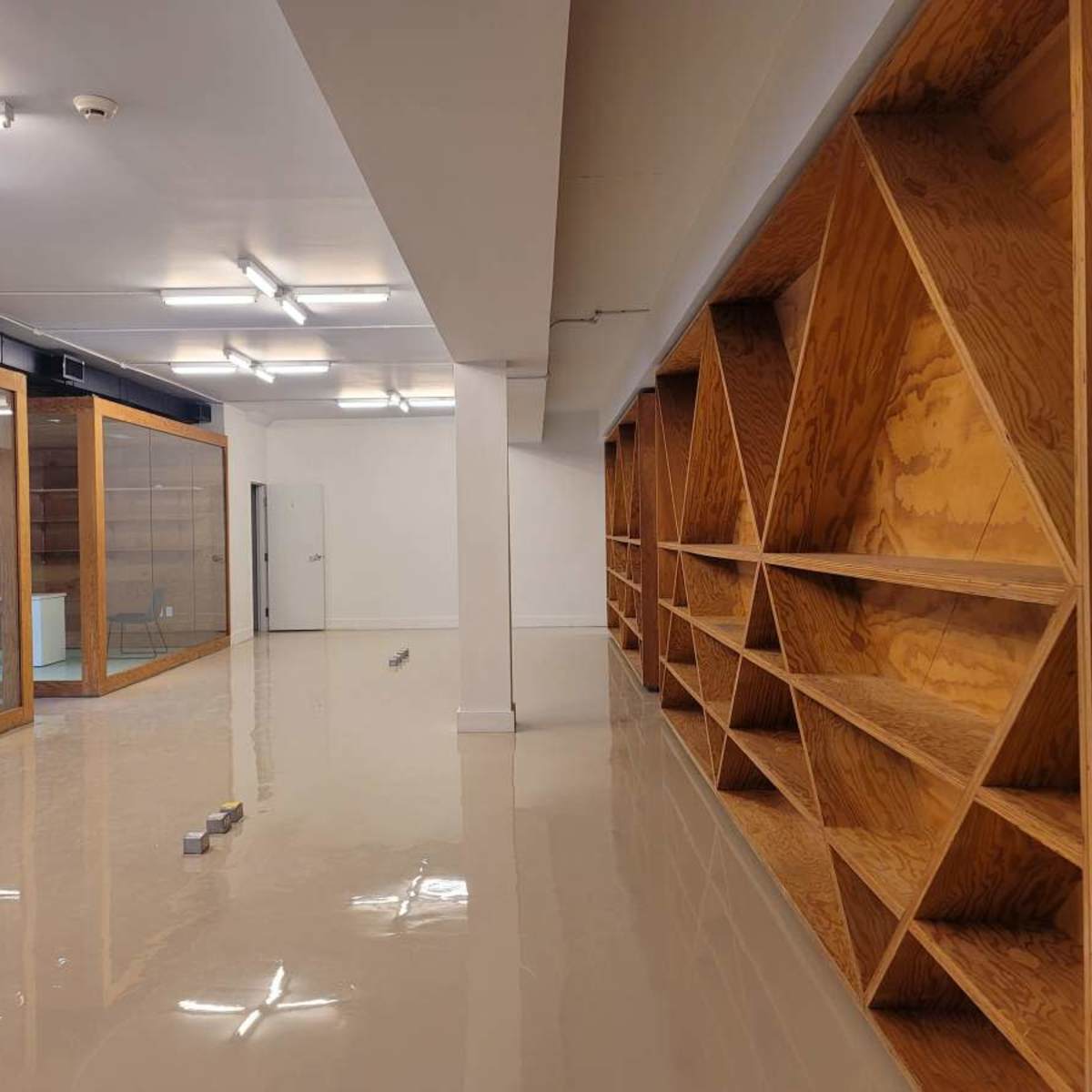 A spacious room with polished floors, wooden shelving units along one wall, and glass-enclosed spaces on the opposite side.