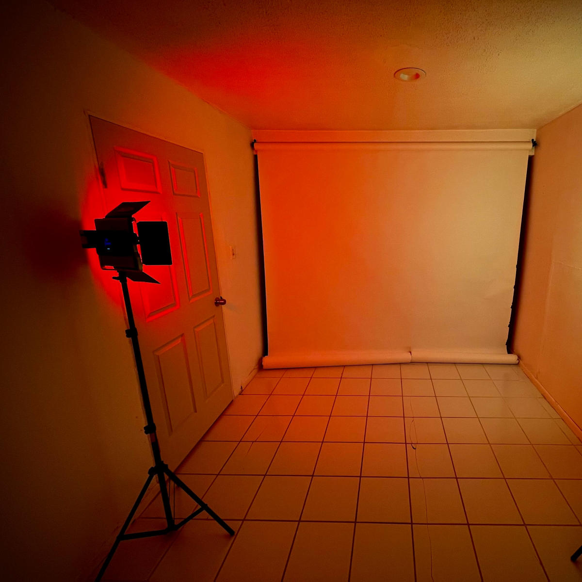 A small room with a blank white backdrop and two studio lights, one red and one green, positioned on either side.