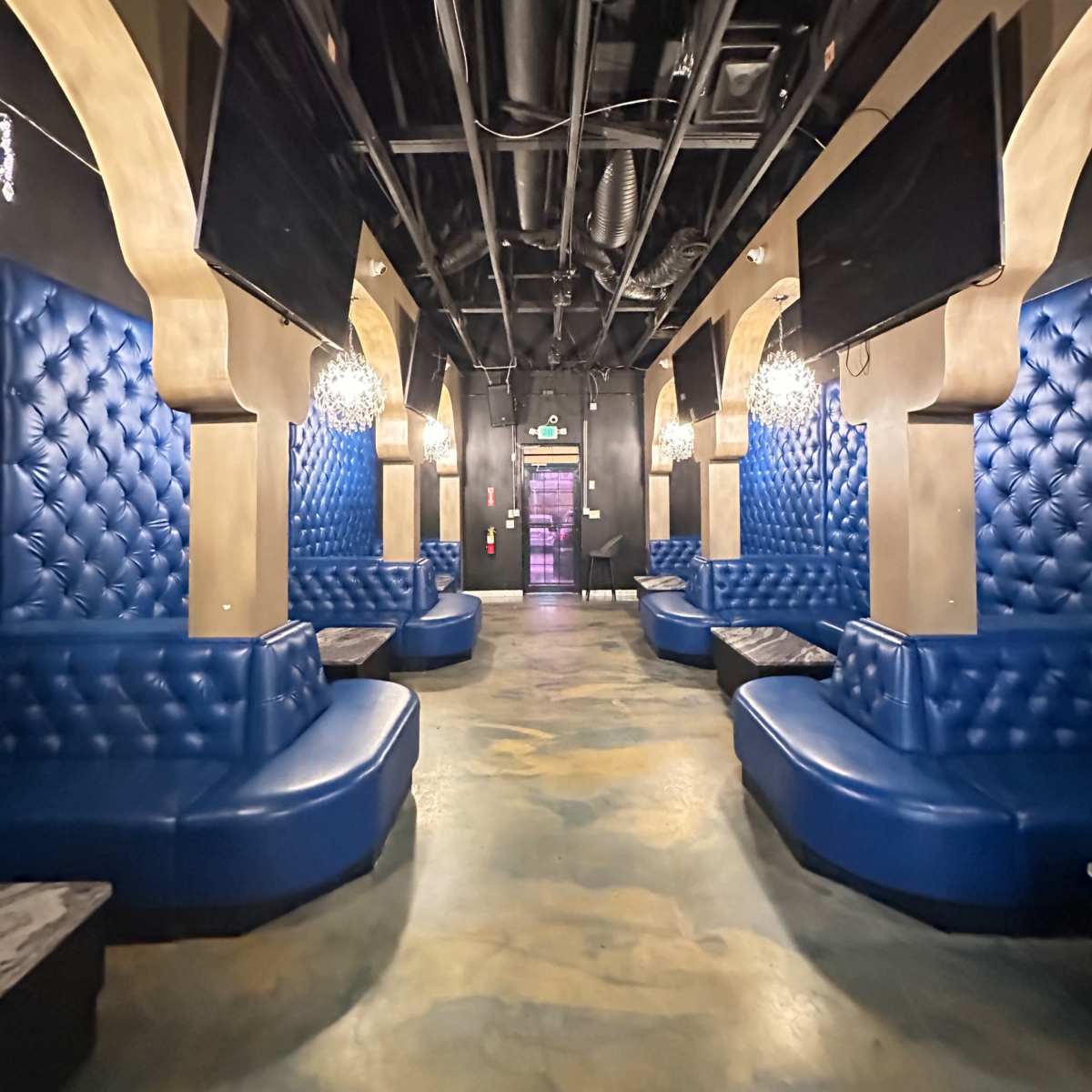 The hallway features long blue leather benches against walls with tufted upholstery, illuminated by pendant lights.