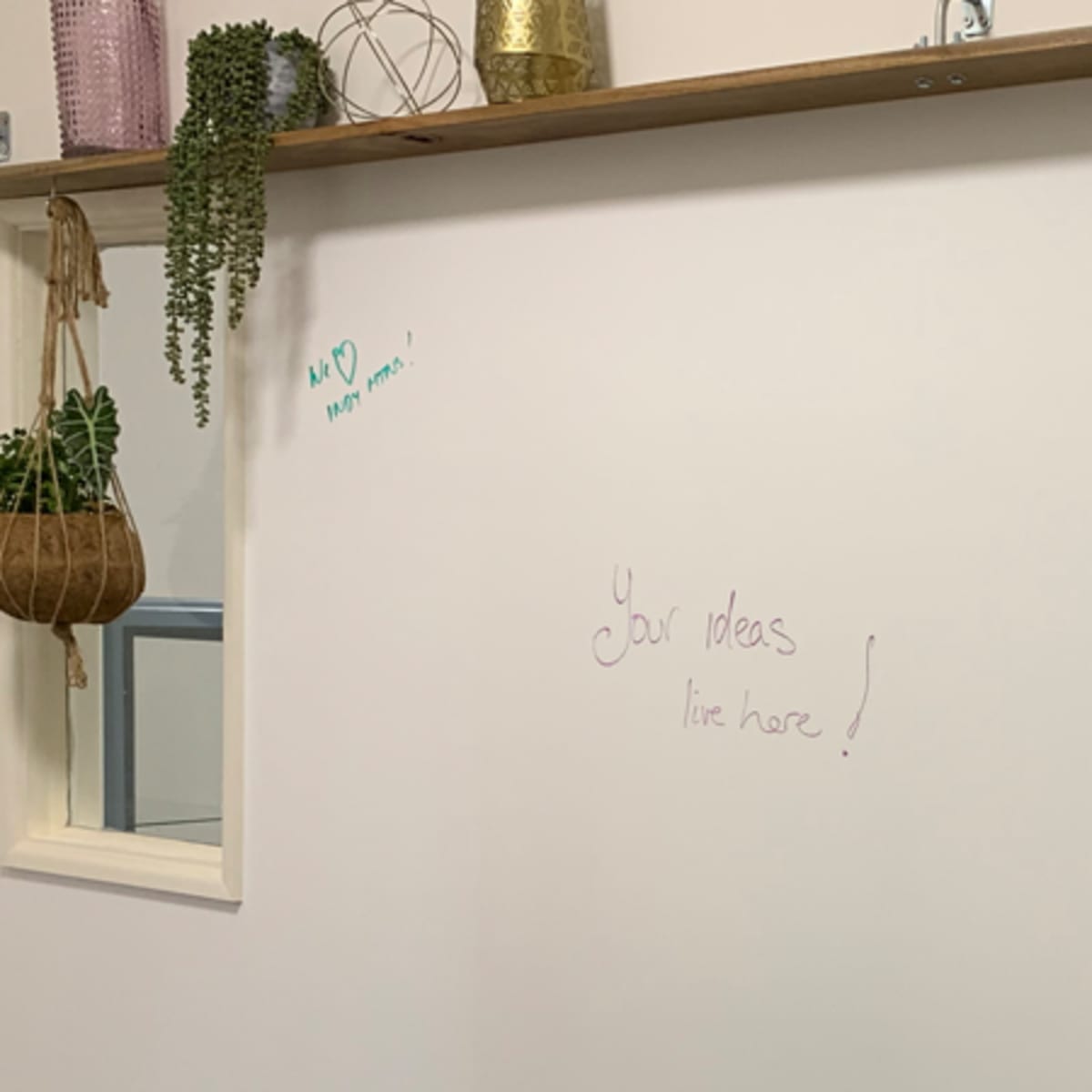 A light-colored wall with a hanging shelf adorned with plants, and a doorway leading to another room with a table and chairs.