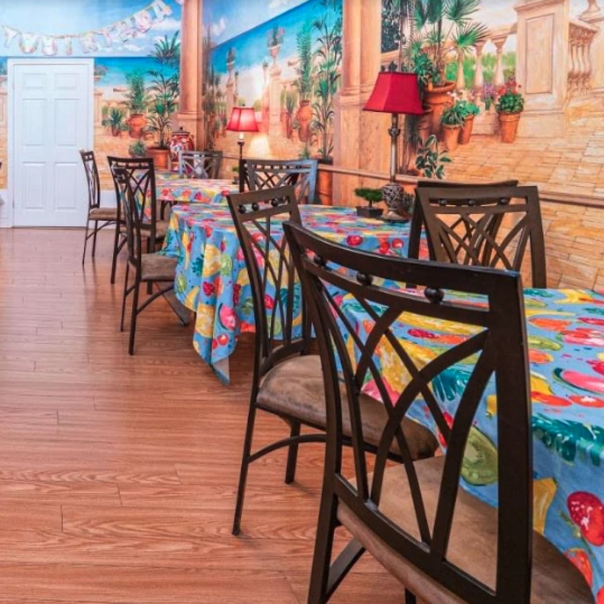 An indoor dining area with multiple tables covered in colorful tablecloths and decorated walls featuring murals.
