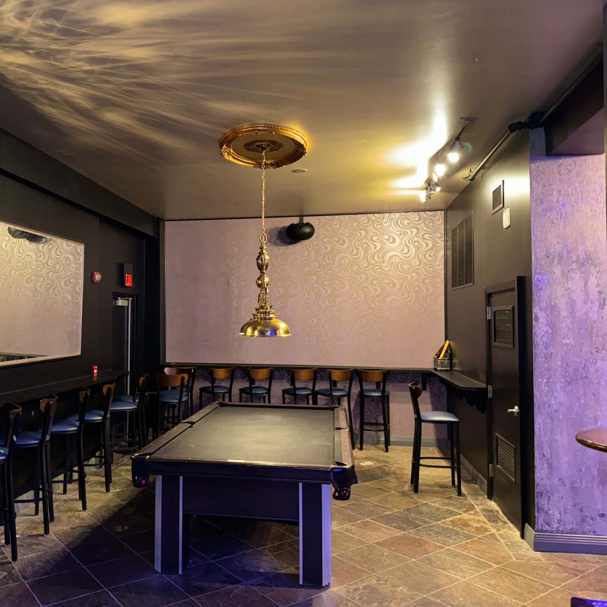 An empty room featuring a pool table in the center, surrounded by bar stools and a wall with mirrors.