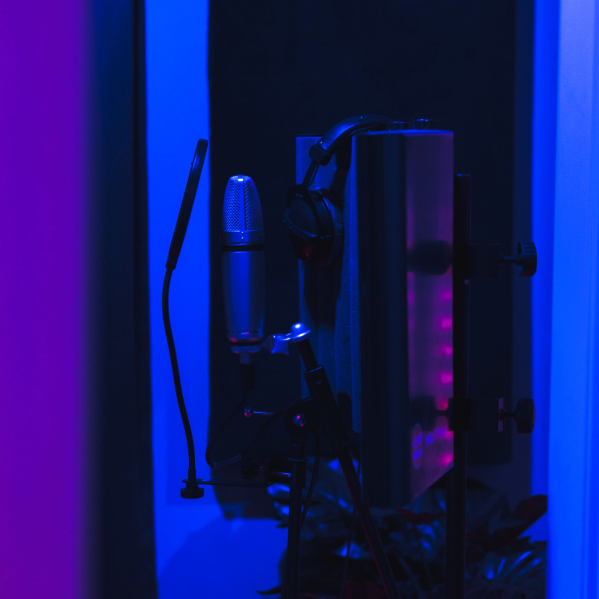 A microphone and audio equipment are positioned in a dimly lit recording studio with blue lighting.