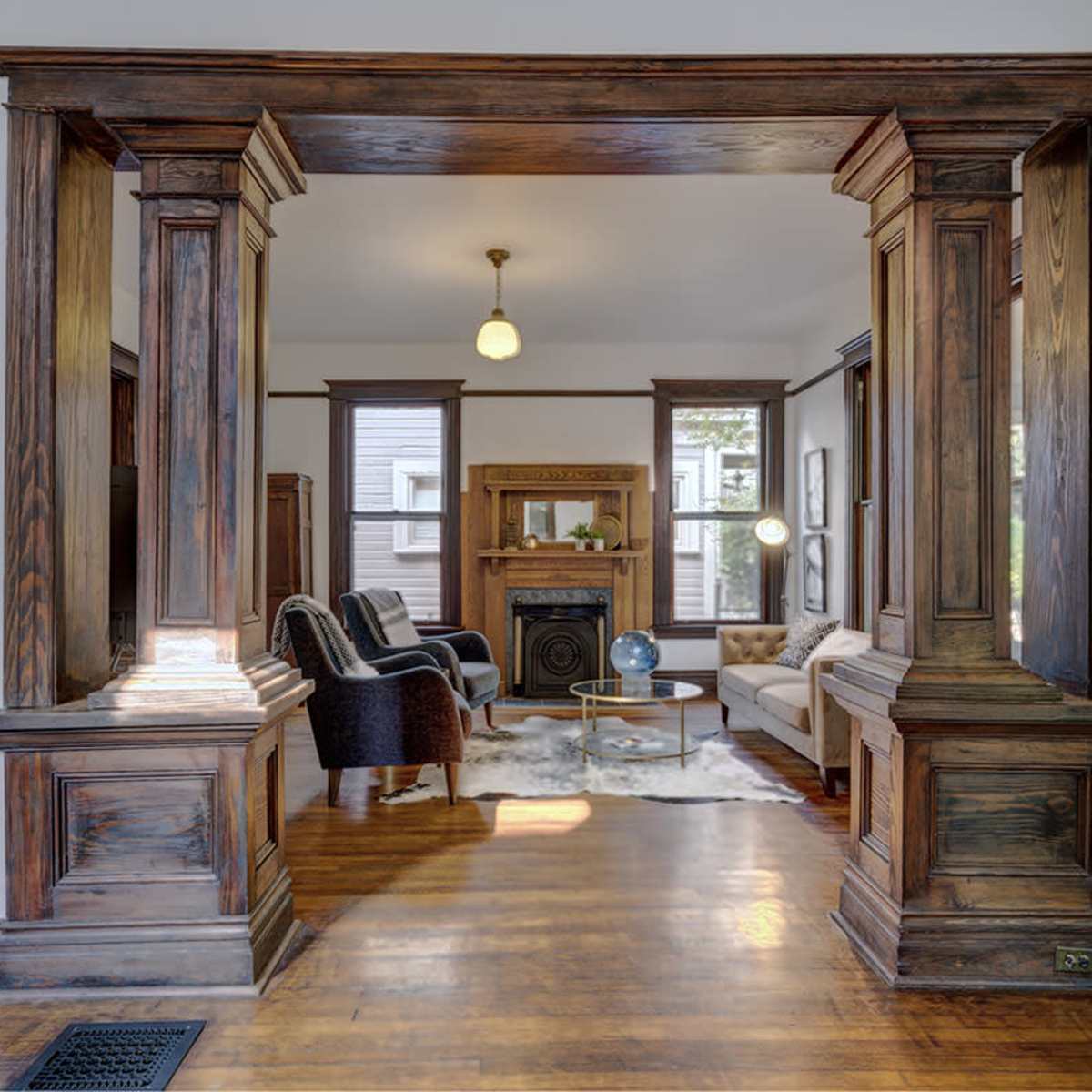 A living room with wooden pillars framing an open entrance, featuring a sofa, chairs, and a fireplace.