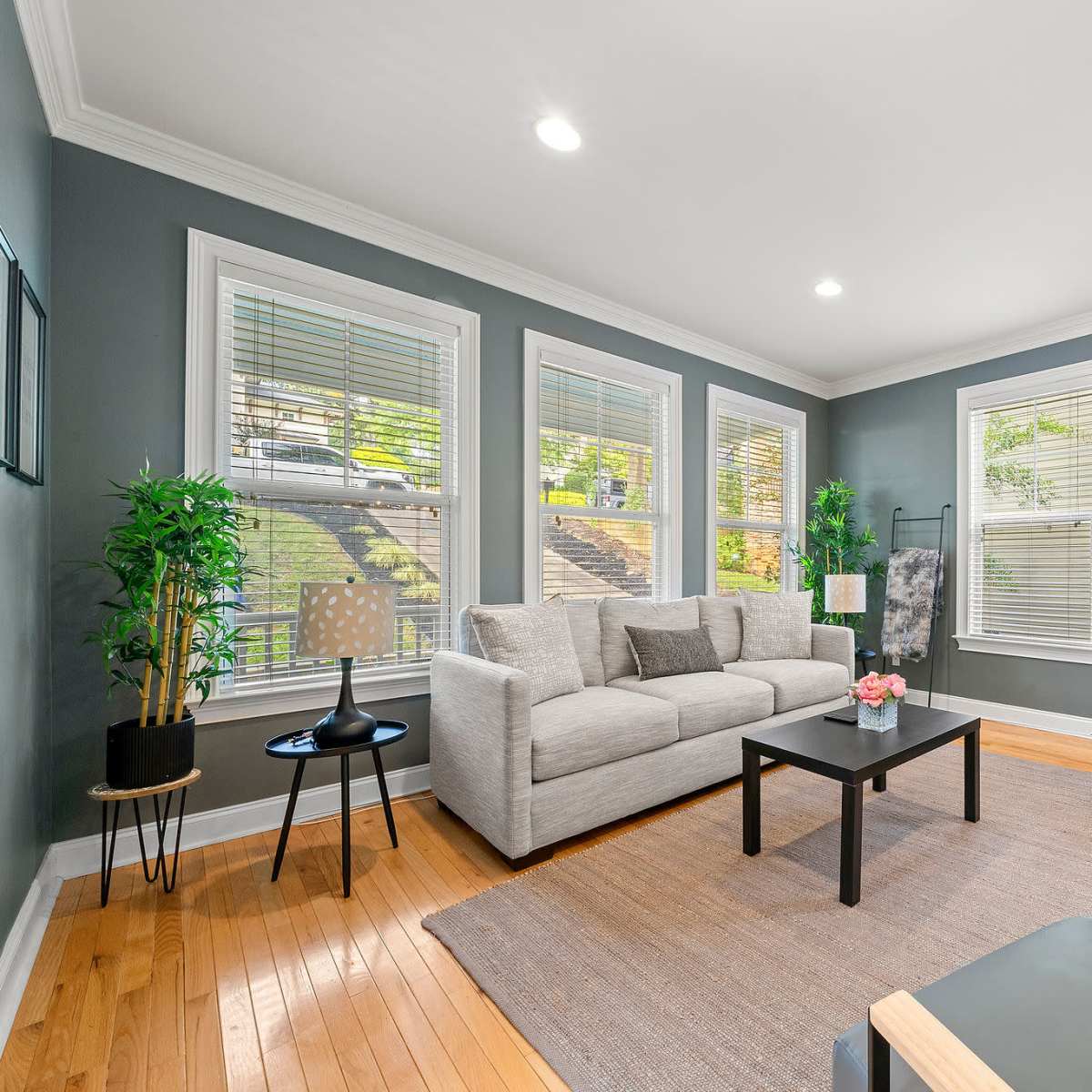 A modern living room with a light gray sofa, two chairs, a black coffee table, and large windows allowing natural light.