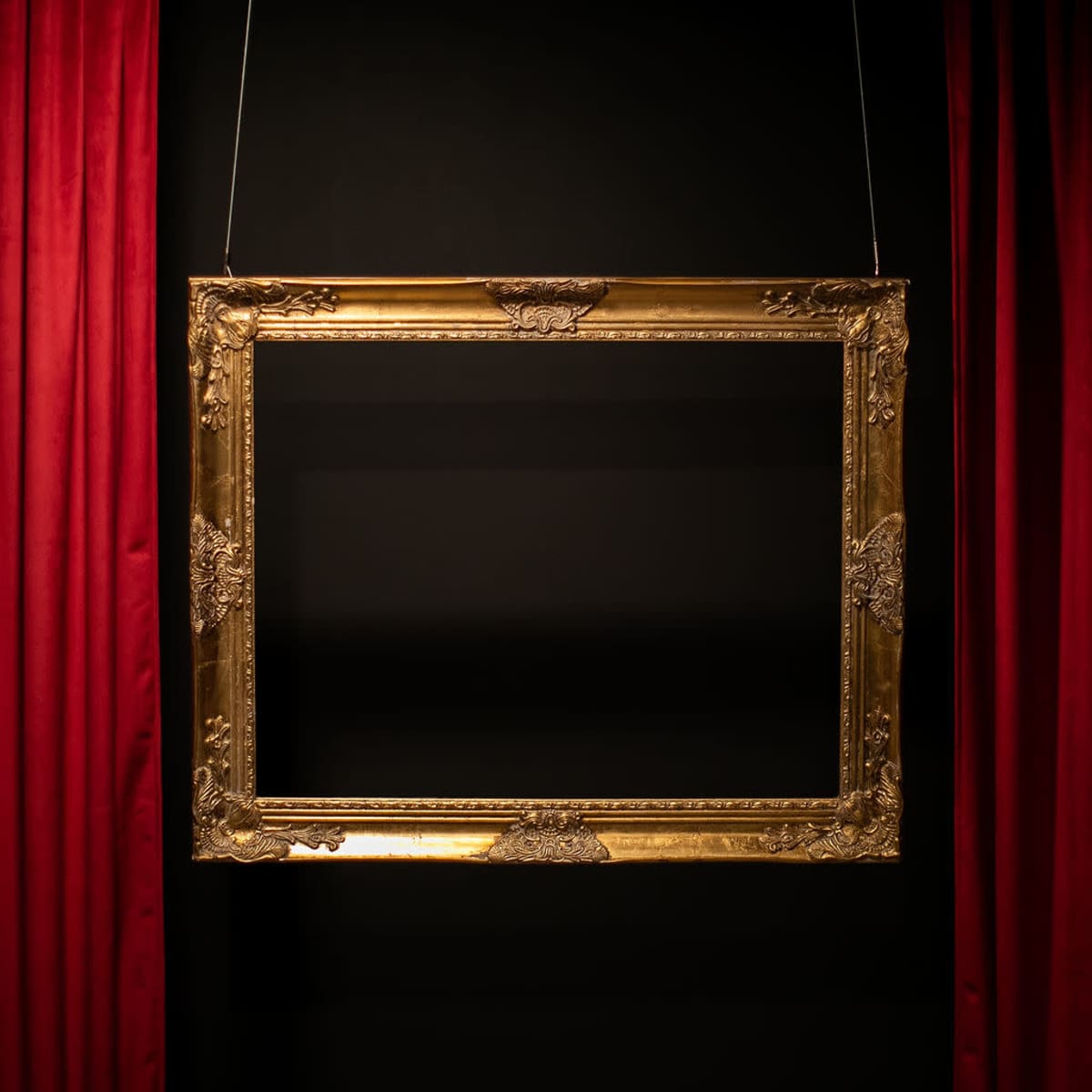 A gold, ornate picture frame hangs against a black wall, flanked by red curtains.
