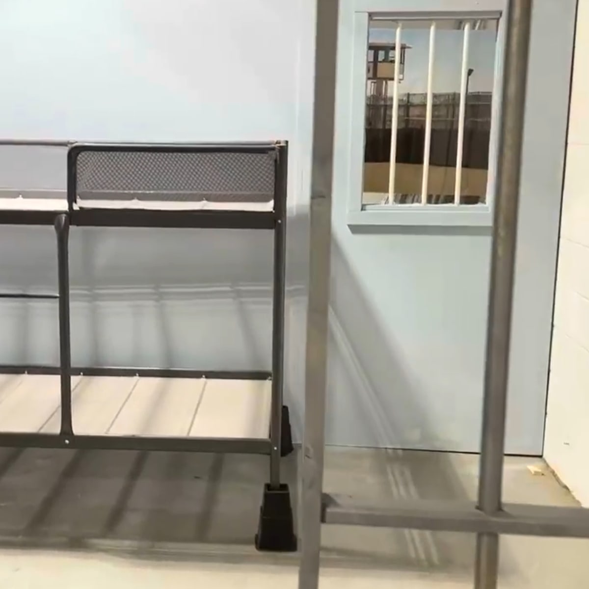 A partially constructed room with a metal frame and a shelving unit against a light blue wall, featuring a barred window.