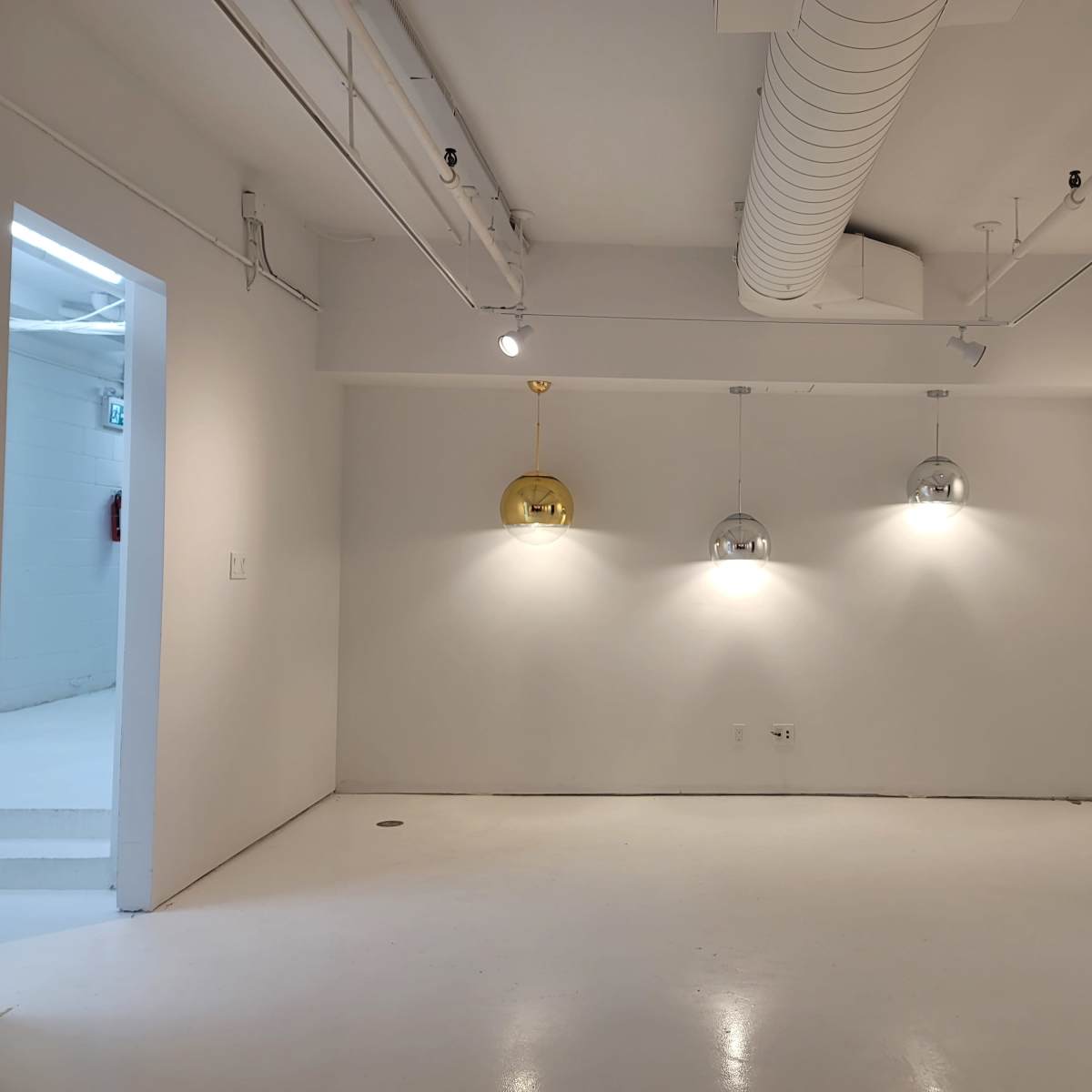A minimalist white room with three pendant lights hanging from the ceiling and a doorway on the left side.
