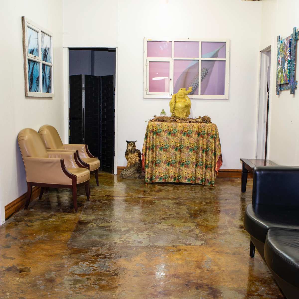 A hallway with two chairs on the left, a table covered with a floral cloth in the center, and an owl sitting beside it.
