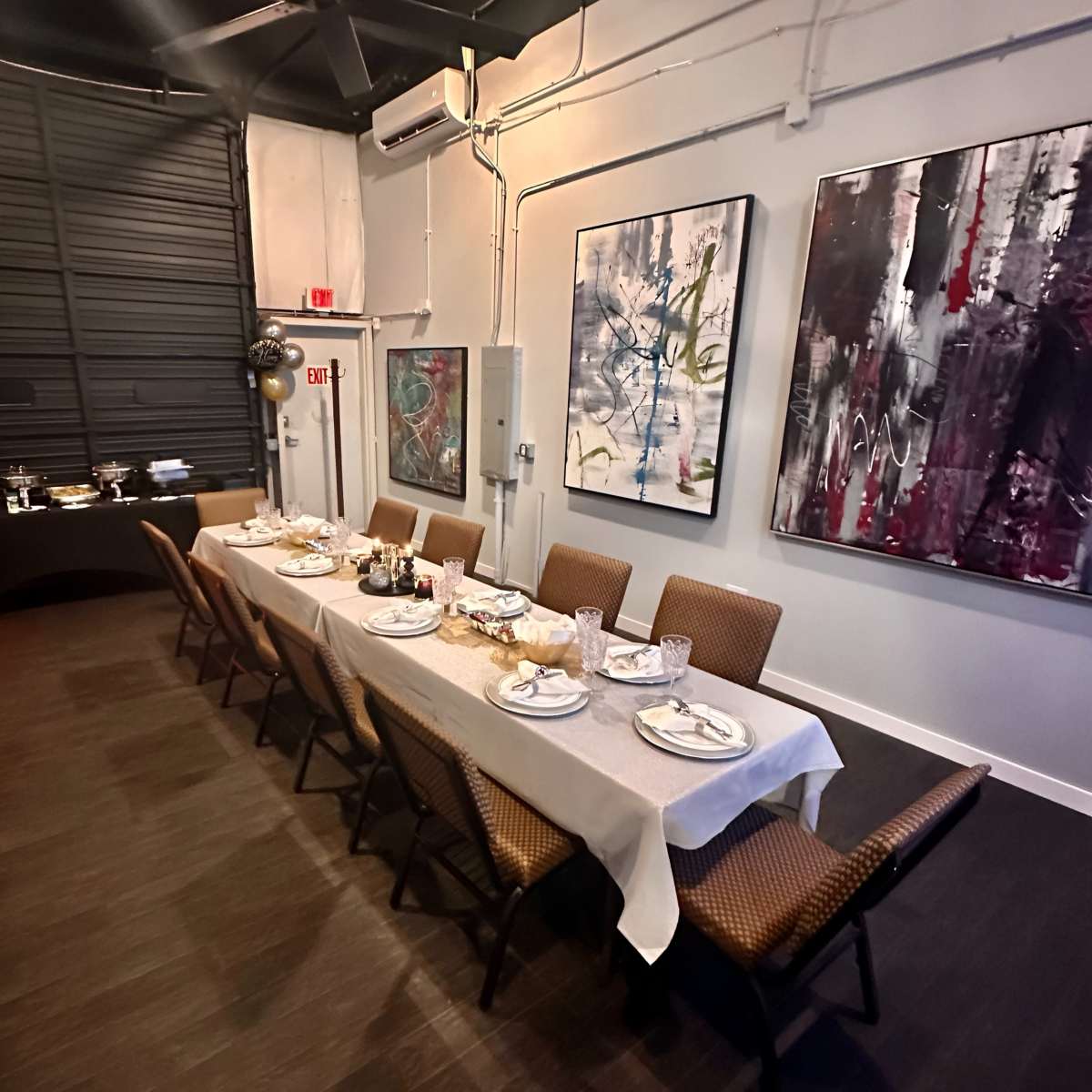 A long dining table is set with plates, utensils, and decorative elements, positioned in a modern room featuring abstract artwork on the walls.