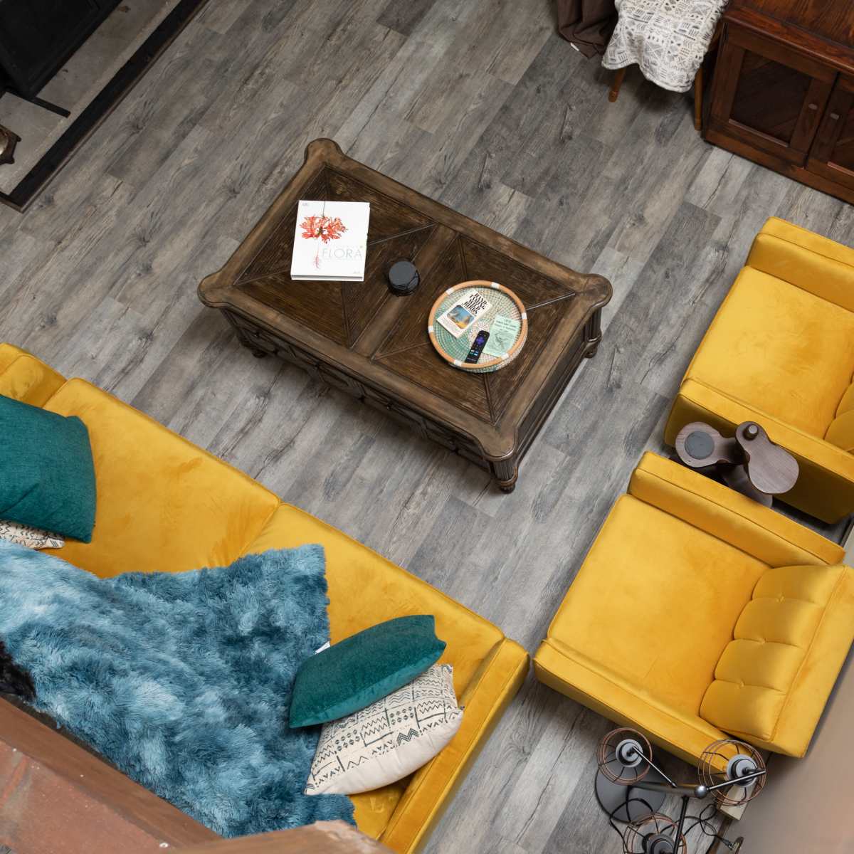 A cozy living room with yellow armchairs, a wooden coffee table, a turquoise throw, and a wooden railing above.