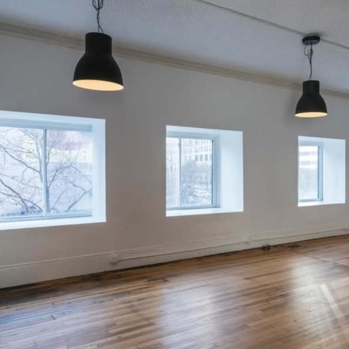 An empty room with four windows and pendant lights hanging from the ceiling.