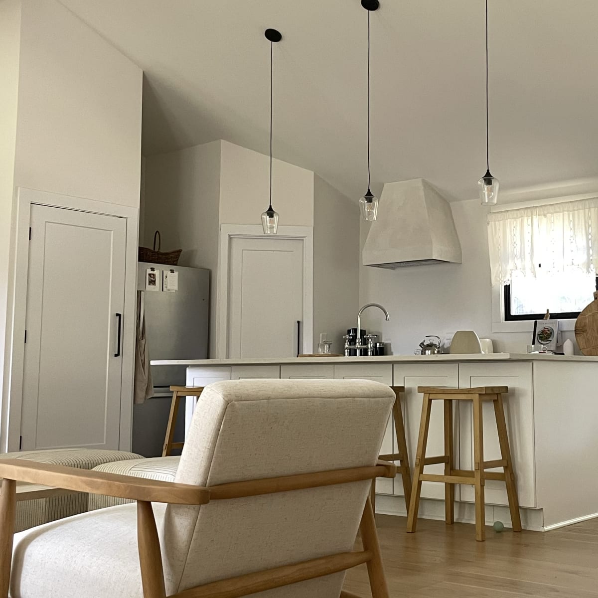 A modern kitchen with white cabinetry, a central island, and wooden stools, illuminated by pendant lights.