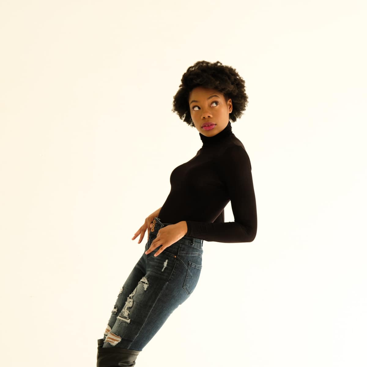 A woman poses in a black turtleneck and ripped jeans while wearing knee-high platform boots.