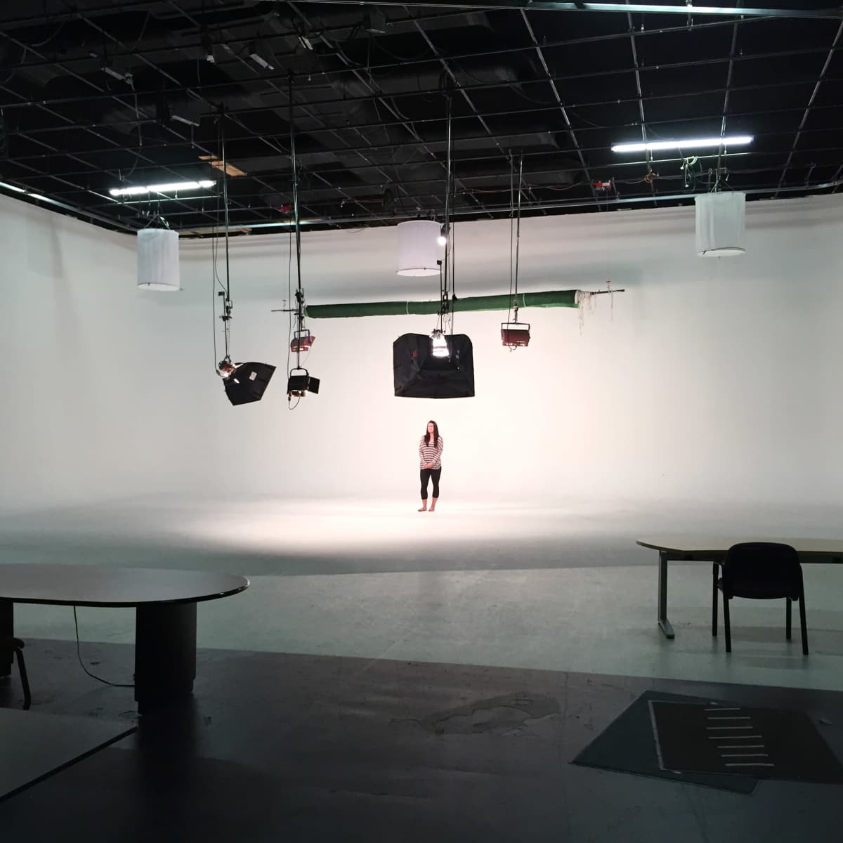 A person stands alone in a spacious, empty studio with a white backdrop and lighting equipment overhead.