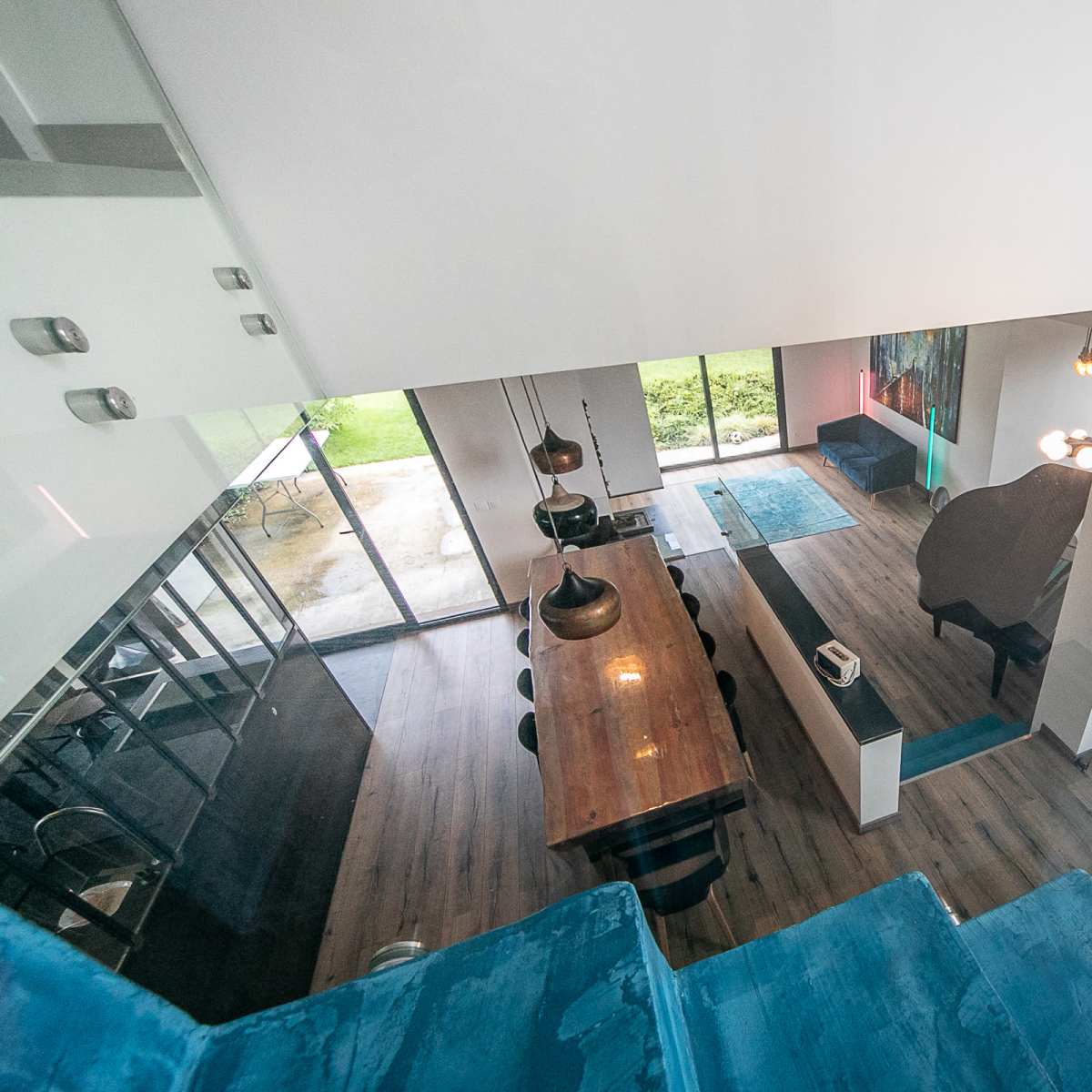 A modern, open-concept home interior with a wooden dining table, black pendant lights, and large glass doors leading to an outdoor area.