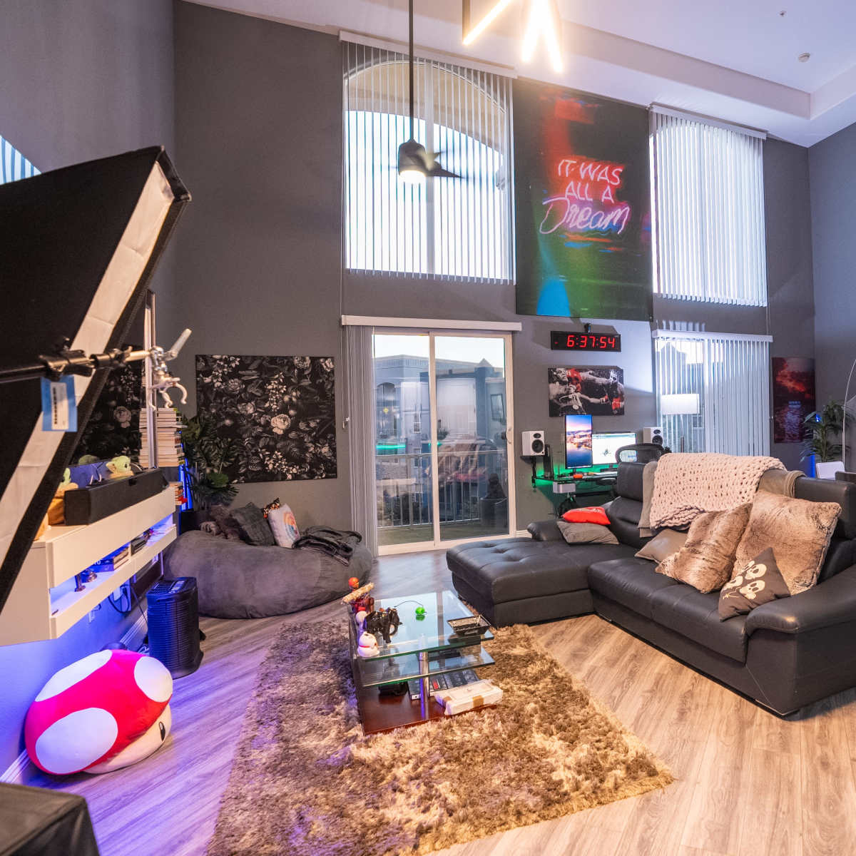 A modern living room with a black leather sofa, a large rug, a workspace with a desk, and colorful decorative elements on the walls.