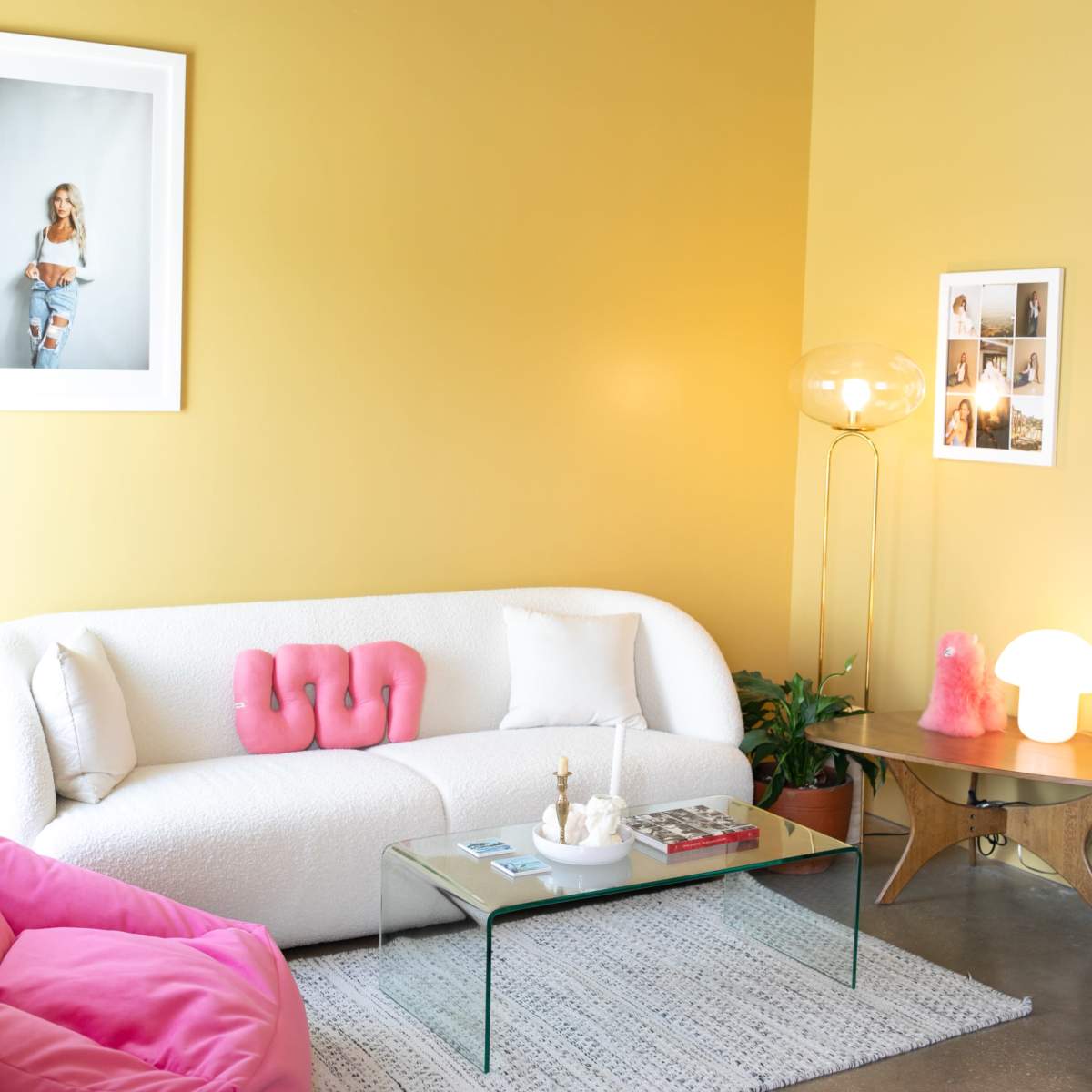 A cozy living room with a white sofa, a glass coffee table, and pink accents, set against a yellow wall and featuring a mix of decorative lighting.
