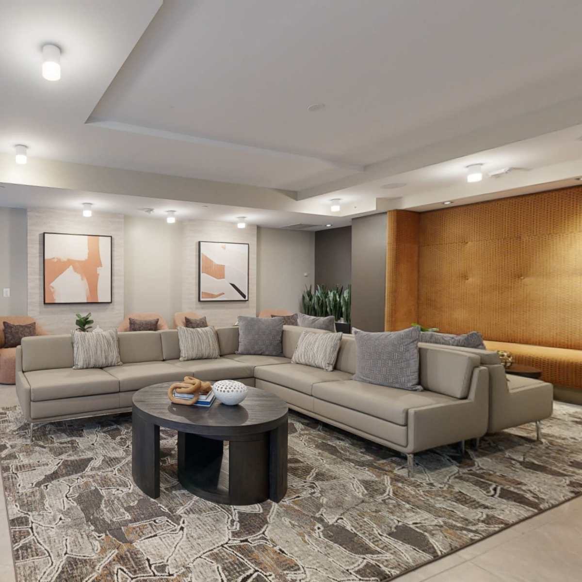 A modern living room with a sectional sofa, a circular coffee table, and artwork on the walls, leading to an open kitchen area.