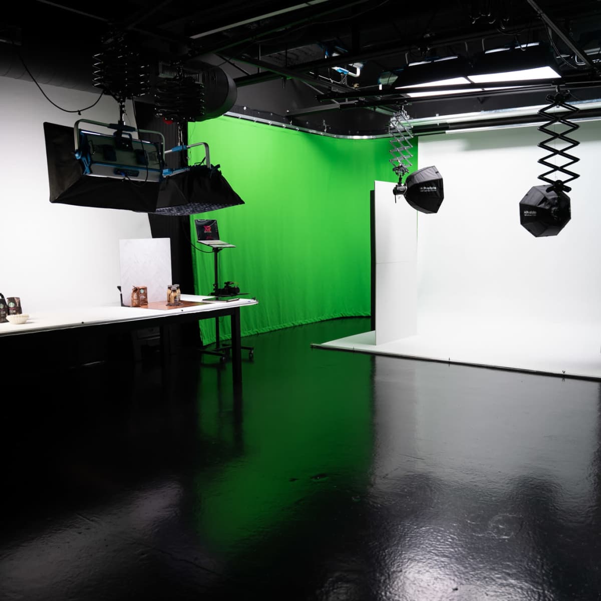 A photography studio features a green backdrop, a white backdrop, and various lighting equipment on a reflective floor.