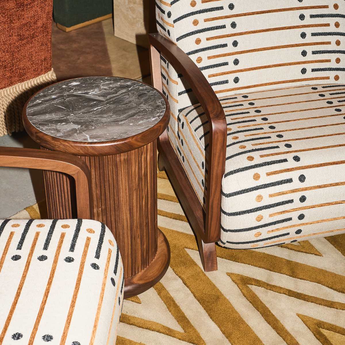 A stylish interior setup featuring two patterned chairs and a cylindrical wooden side table with a marble top, placed on a geometric area rug.