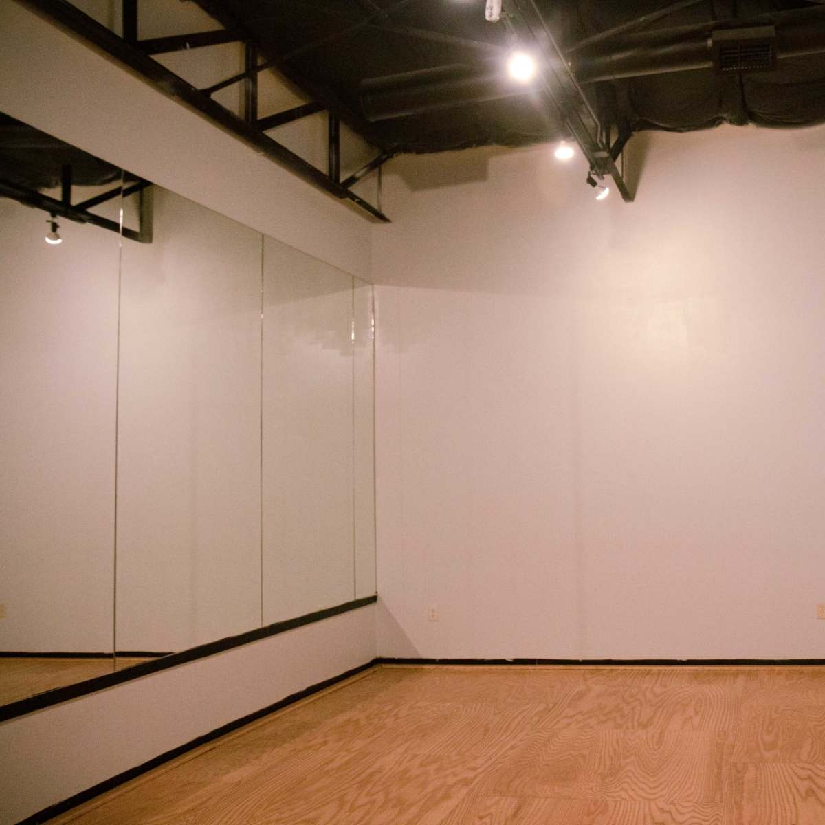 A spacious dance studio with wooden flooring, a wall-mounted ballet bar, and a large mirror.
