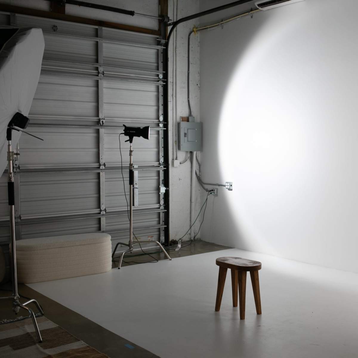 A photography studio with a wooden stool in front of a plain white backdrop, illuminated by studio lights.