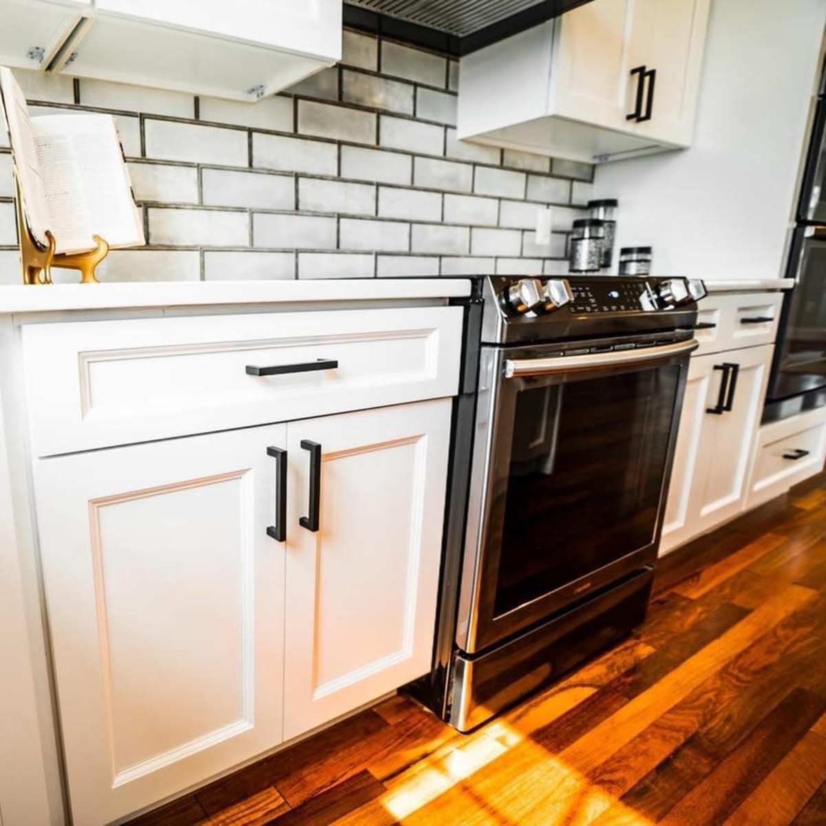 A modern kitchen with white cabinets, a stainless steel stove, and gray tiled backsplash.