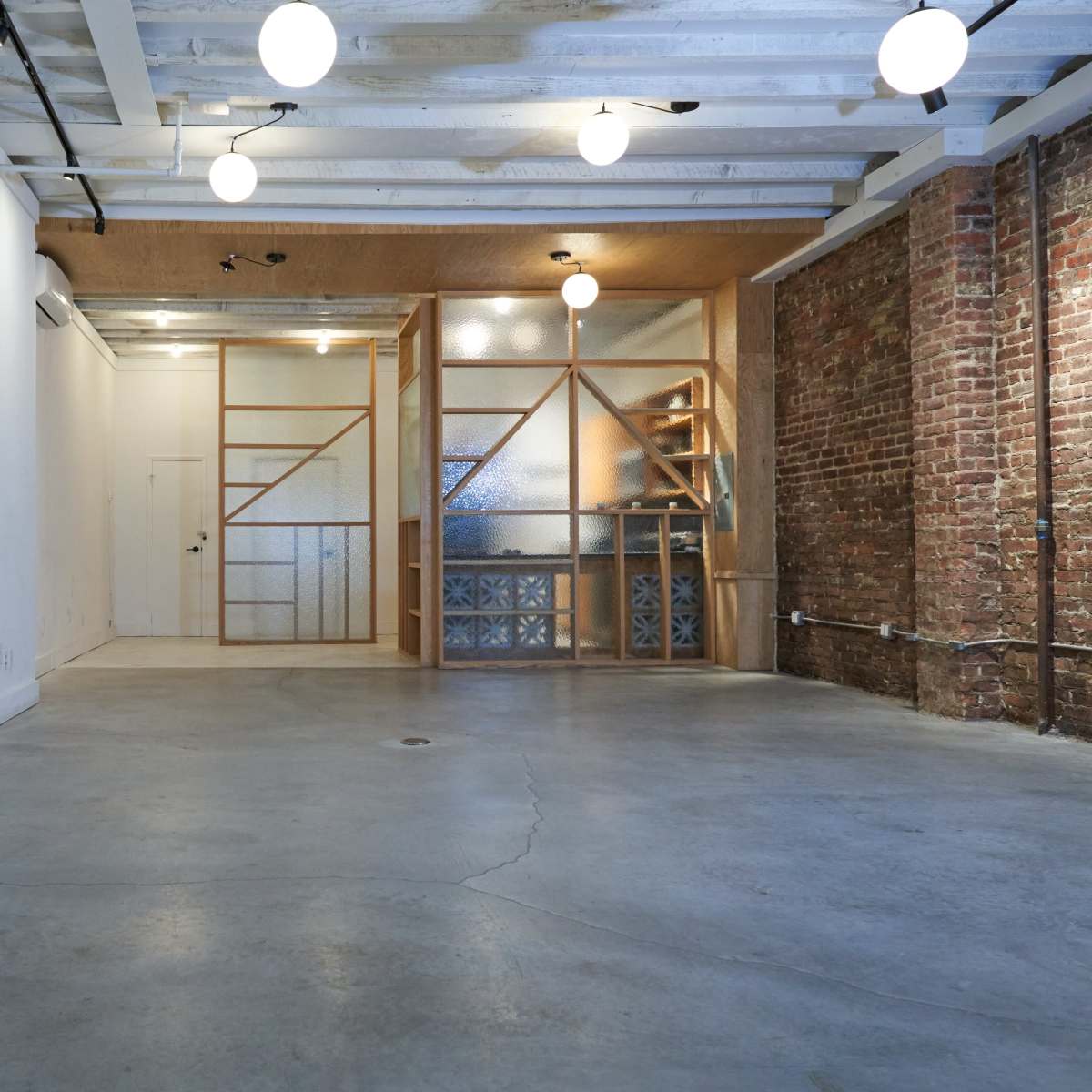 A spacious interior with concrete flooring, exposed brick walls, and a wooden partition with a glass design separating two areas.