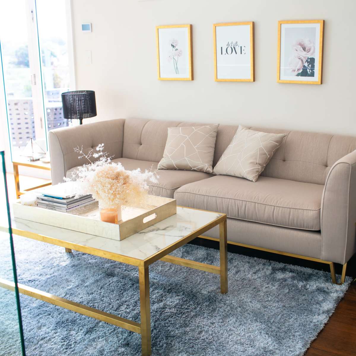 A modern living room features a beige couch with two cushions, a marble-top coffee table, and framed artwork on the wall.