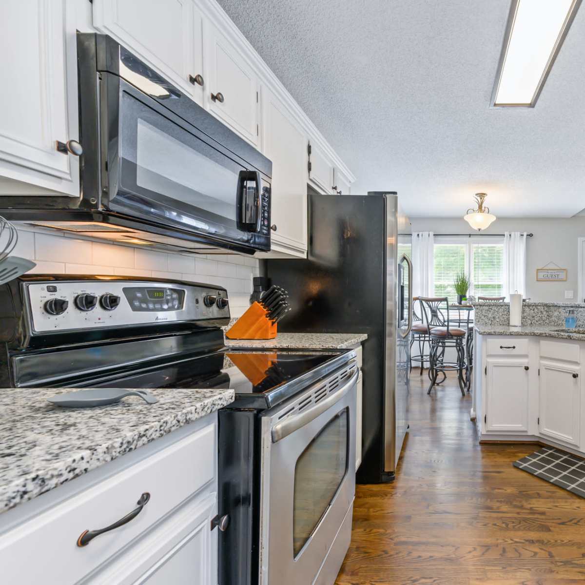 A kitchen features white cabinets, stainless steel appliances, granite countertops, and hardwood floors.