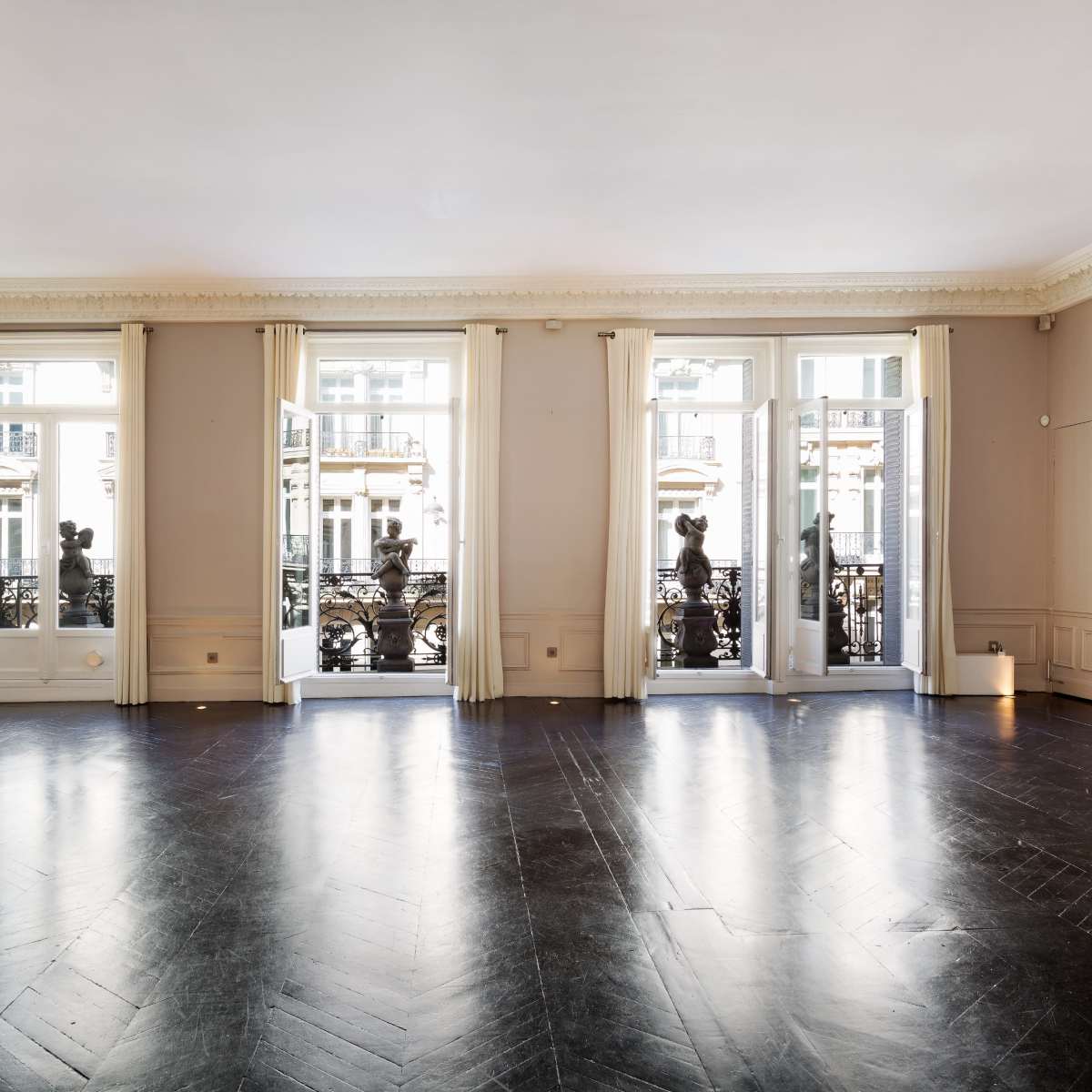 An empty room with dark wooden flooring and large windows that open to a balcony.